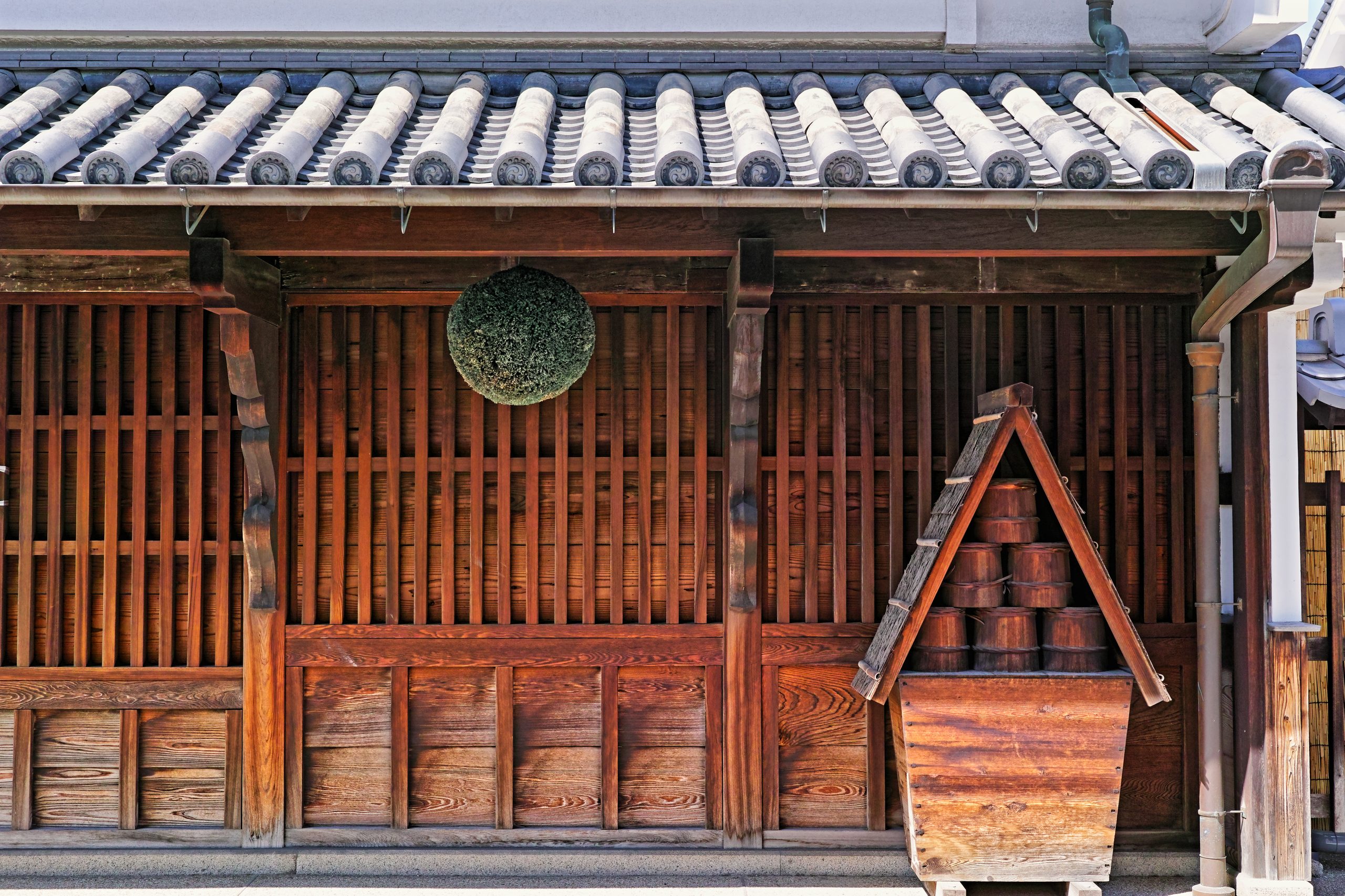 The dark timber lattice front of an old merchant house under a tiled roof, a cedar ball hung above the door