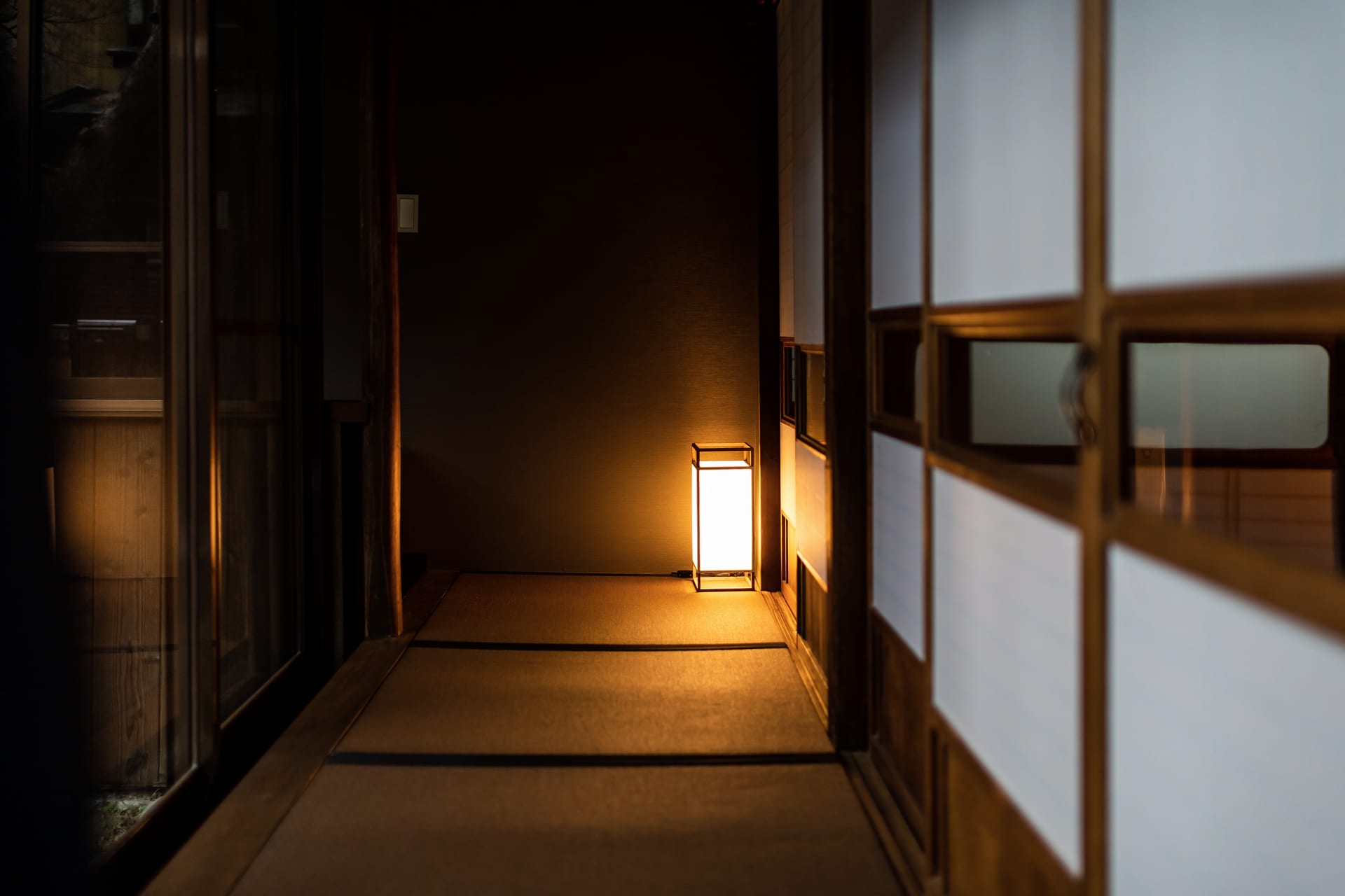 A dim wooden corridor in an old ryokan, lit by a single paper lantern