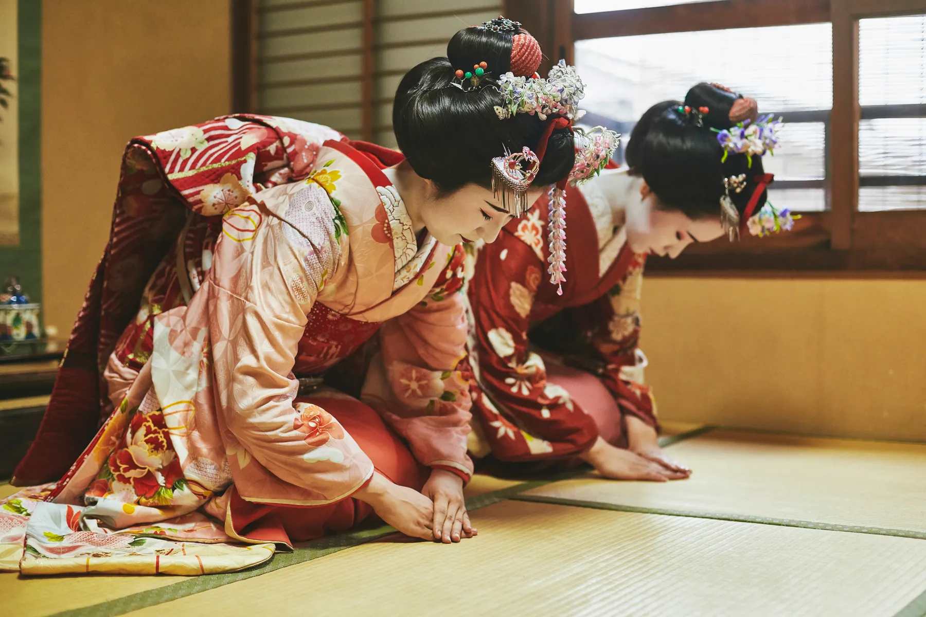 Two maiko in kimono kneeling on tatami, bowing