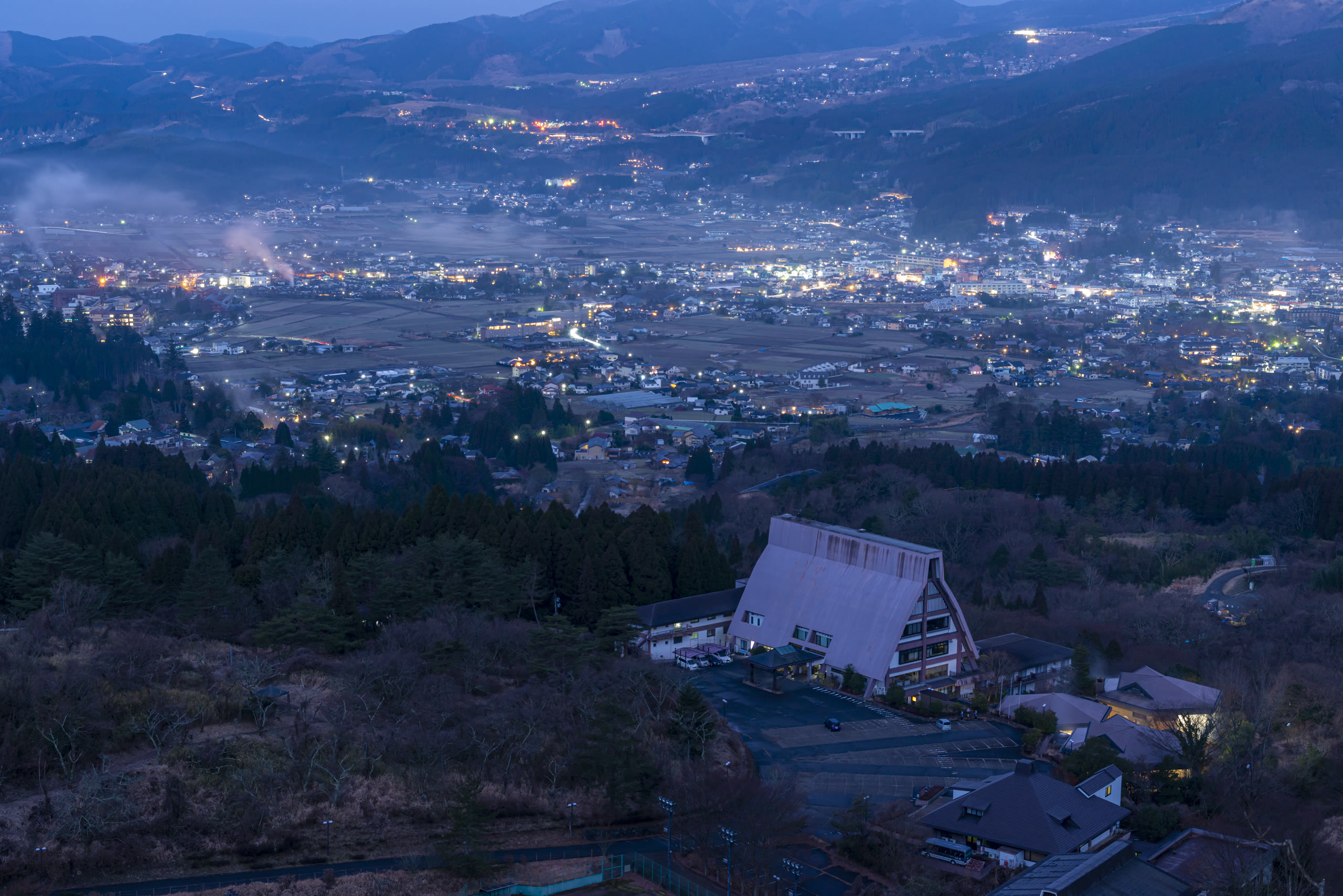 Steam rising over an onsen town in a Kyushu valley at dusk