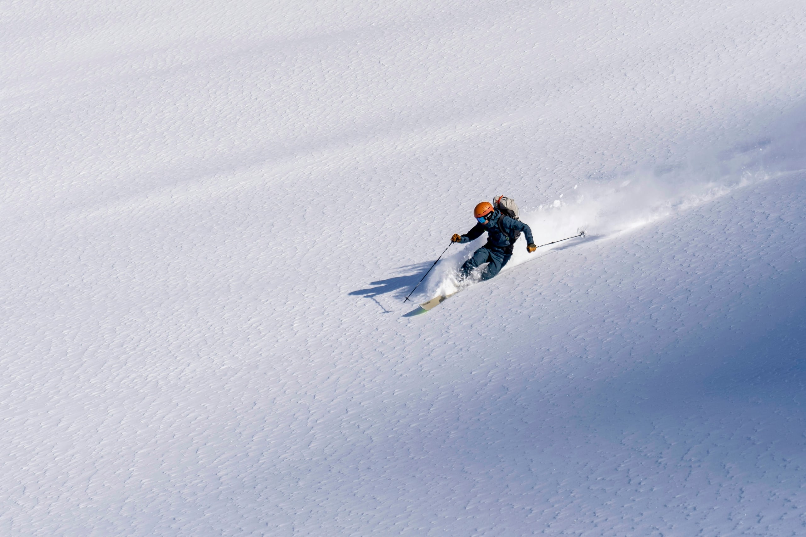 A lone skier carving down a wide slope of untouched powder in Hokkaido