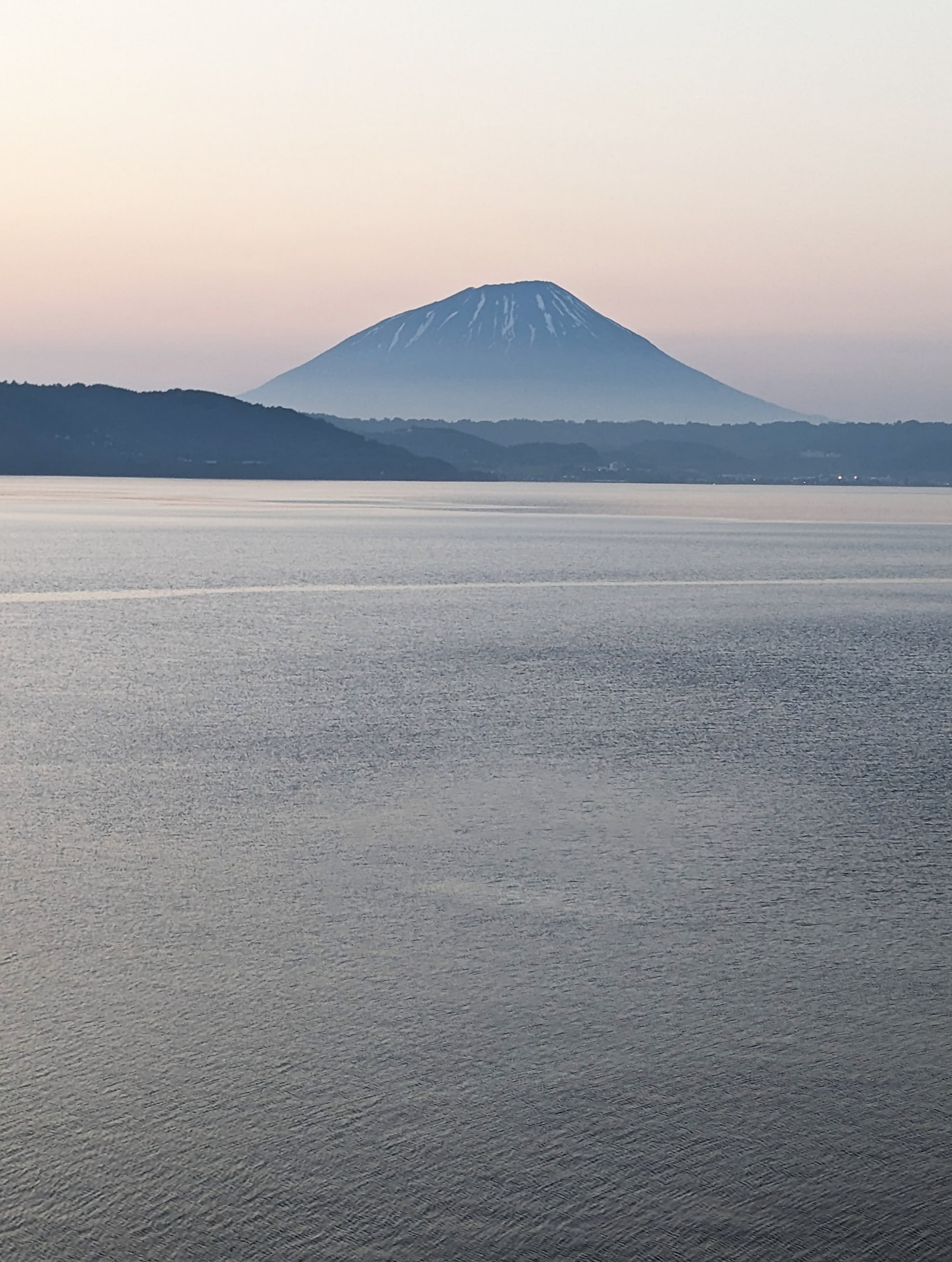 Mount Yotei rising beyond the calm grey water of Lake Toya in the evening light