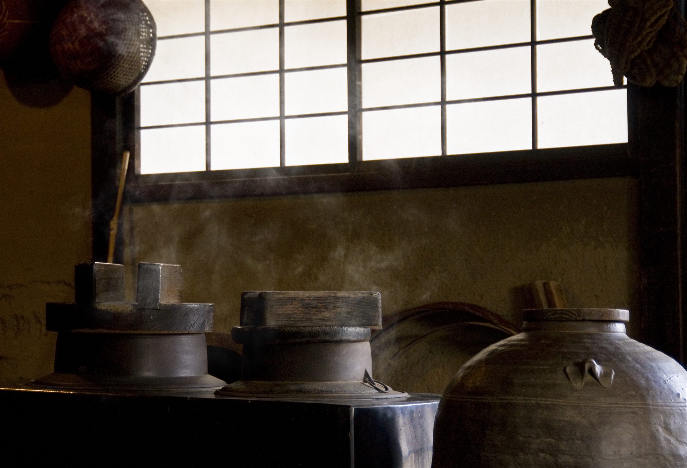 Old wooden brewing vats and a large ceramic jar in a Kyoto sake brewery
