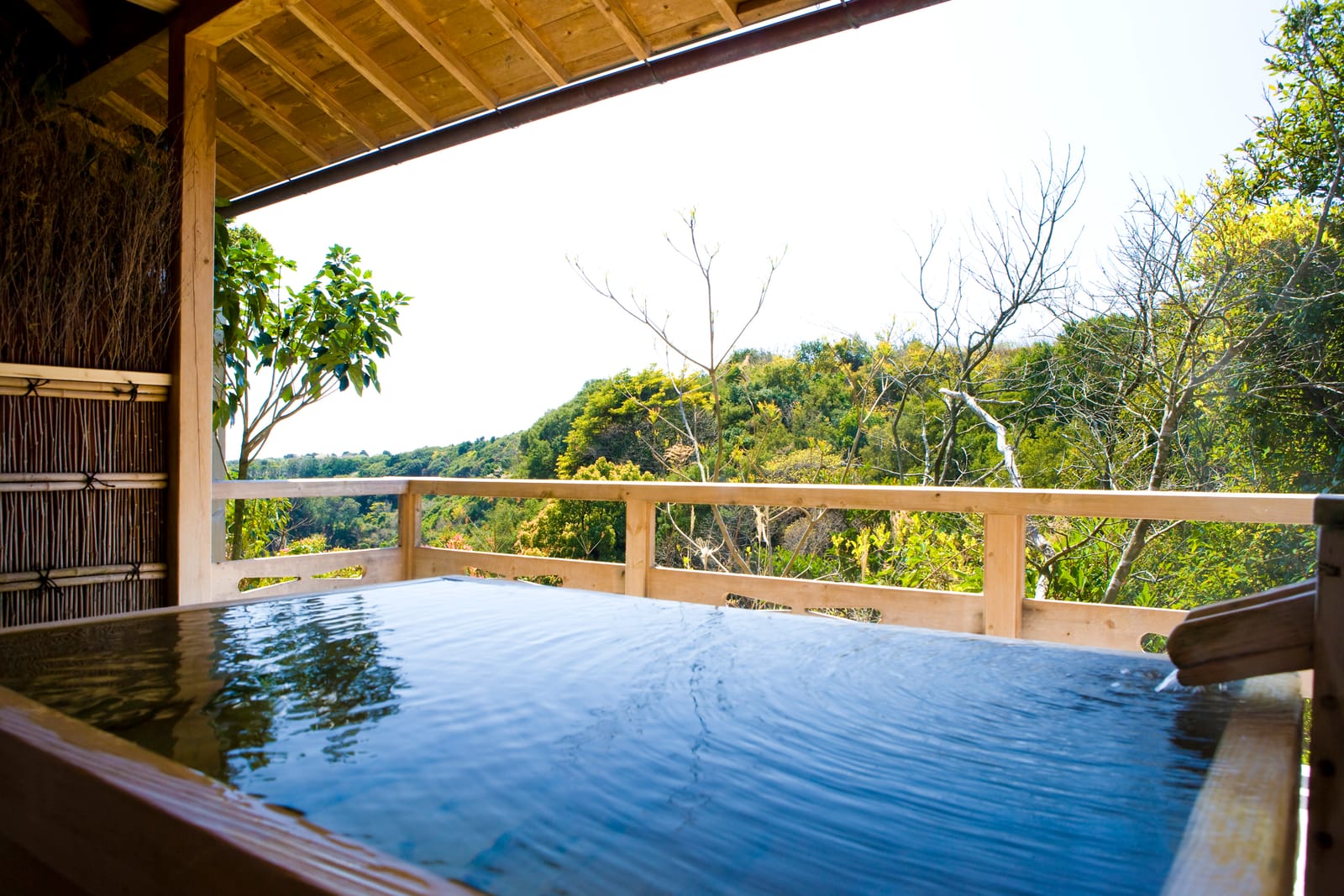 A private open-air onsen bath on a wooden deck overlooking a wooded hillside