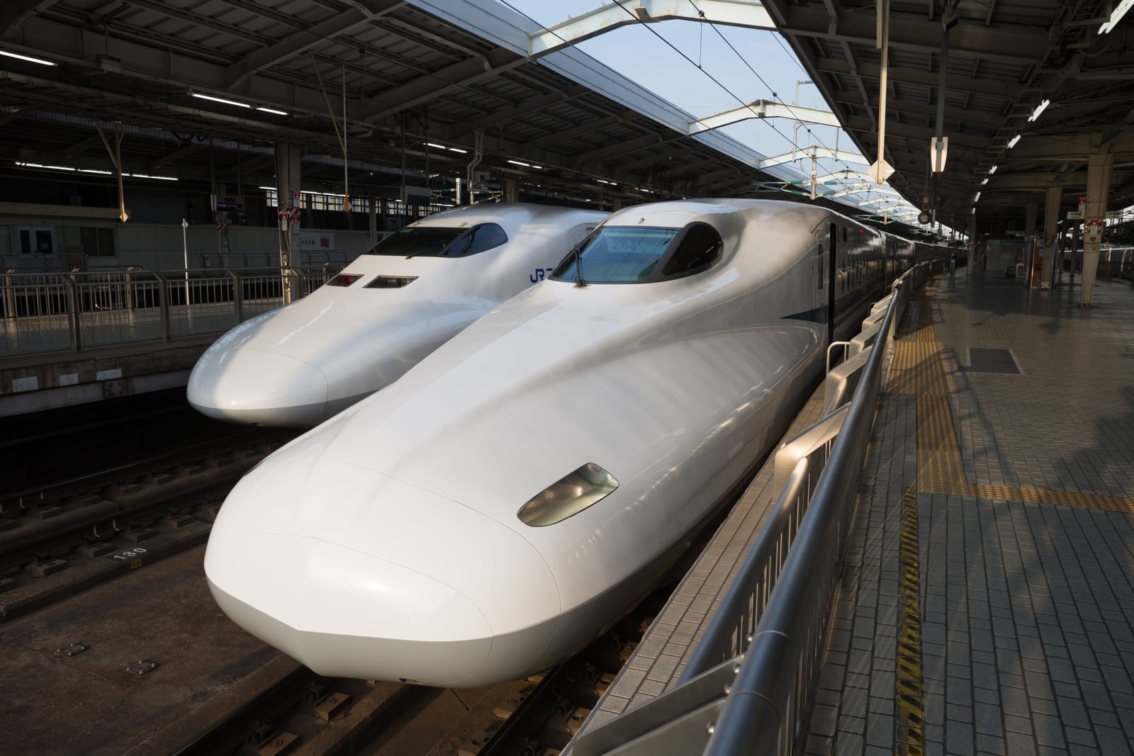 Two white shinkansen bullet trains at a station platform in morning light