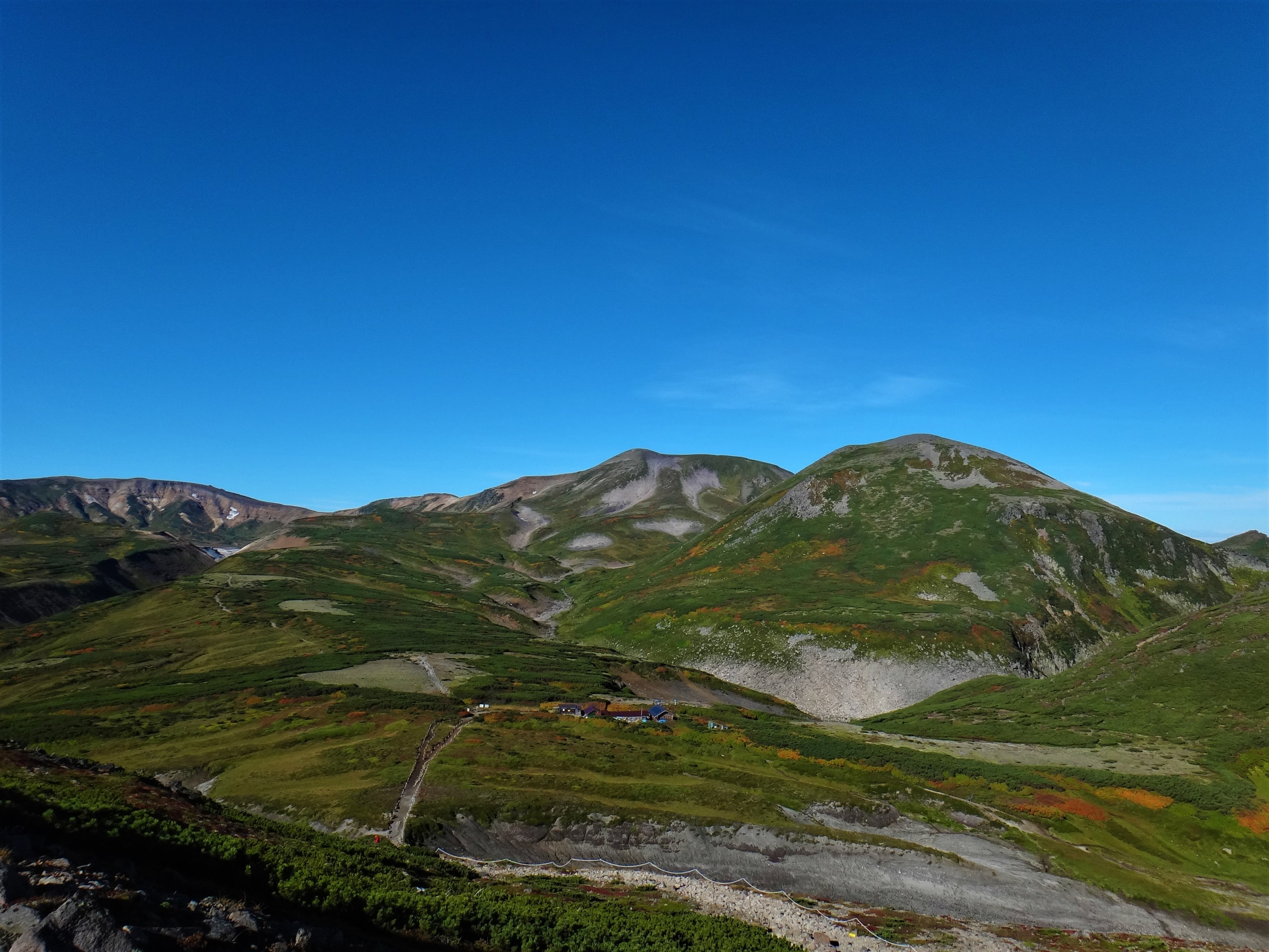 Sugatami pond below Asahidake, white steam rising from the fumaroles on the mountain's flank above green alpine slopes, Daisetsuzan National Park