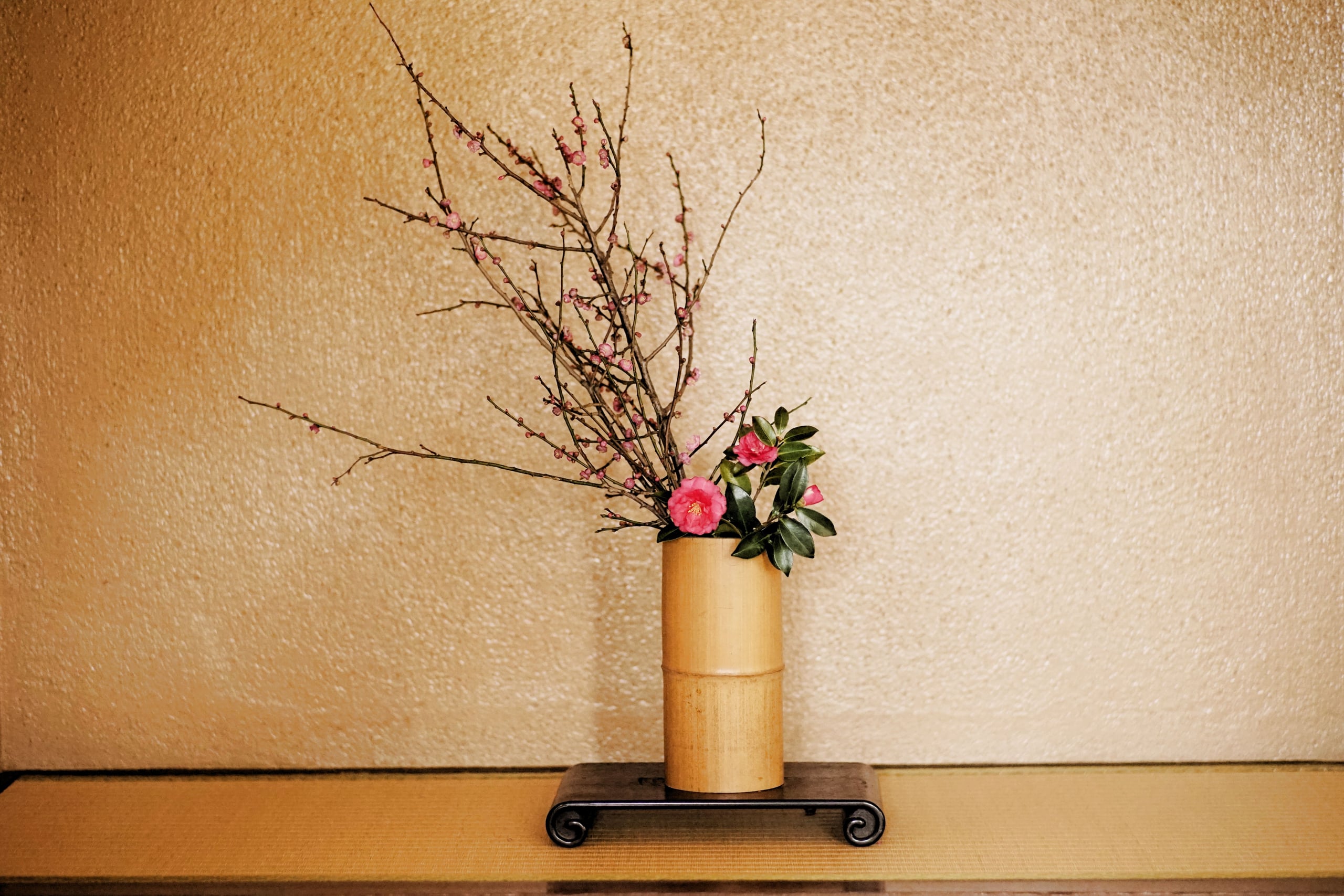 An ikebana arrangement of pink plum blossom branches and a camellia in a bamboo vase