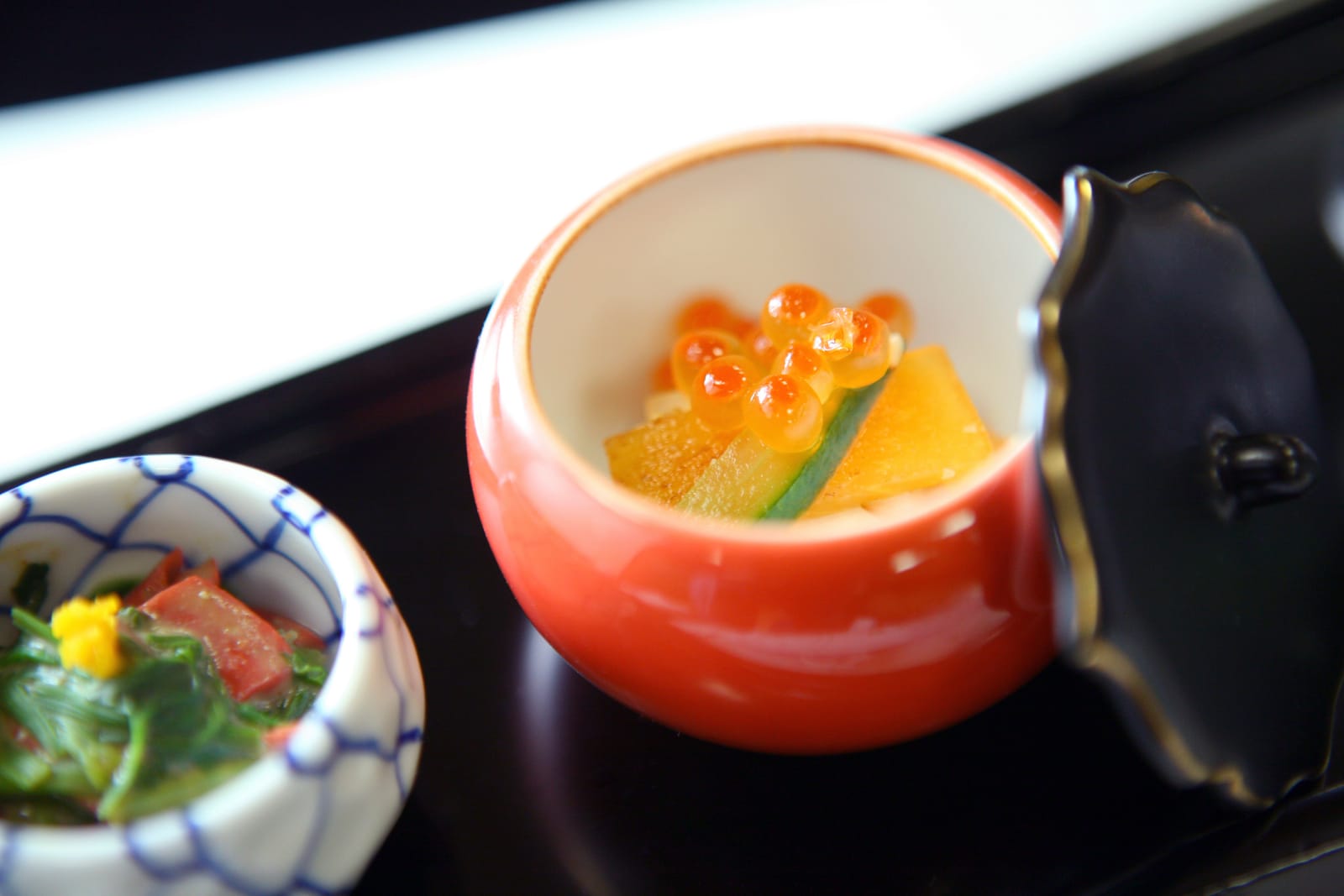 A single kaiseki course in a small red lacquer cup, salmon roe over pickled cucumber and daikon set on ice