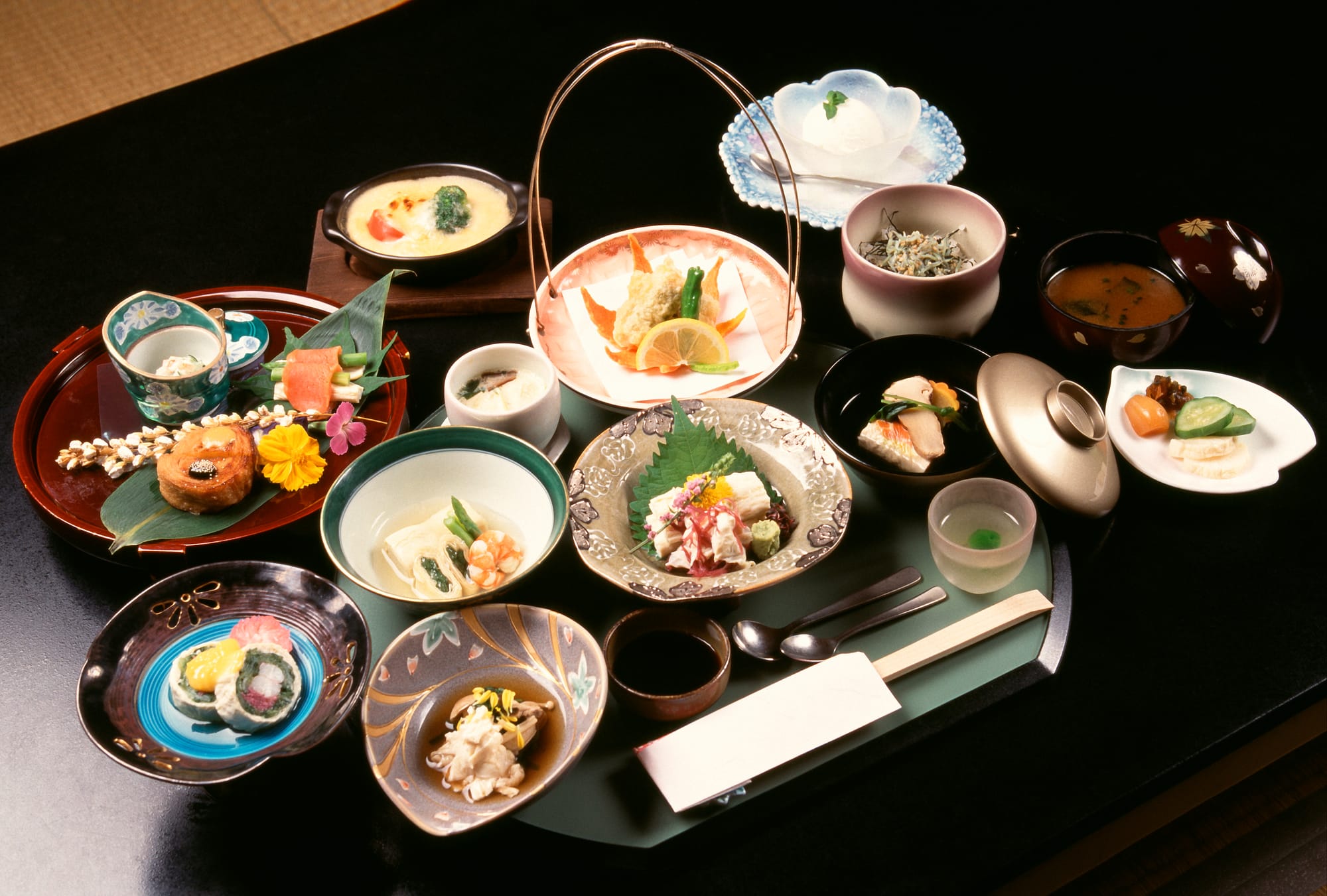 A full kaiseki course spread across a black lacquer table, a dozen small dishes in patterned bowls and plates each holding a single composed course