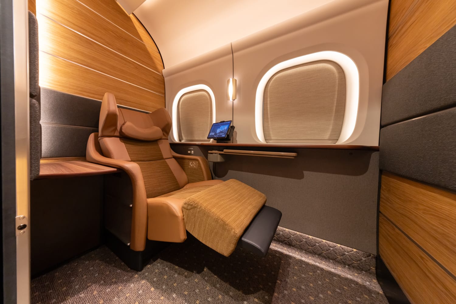 The single Supreme Class cabin in car 10: a tan leather seat reclined with its padded leg rest raised, a tablet on the ledge beneath a softly lit rounded window, wood-panelled walls