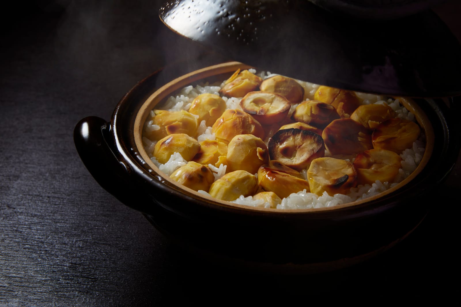 Steam rising from chestnut rice cooked in a dark ceramic donabe pot