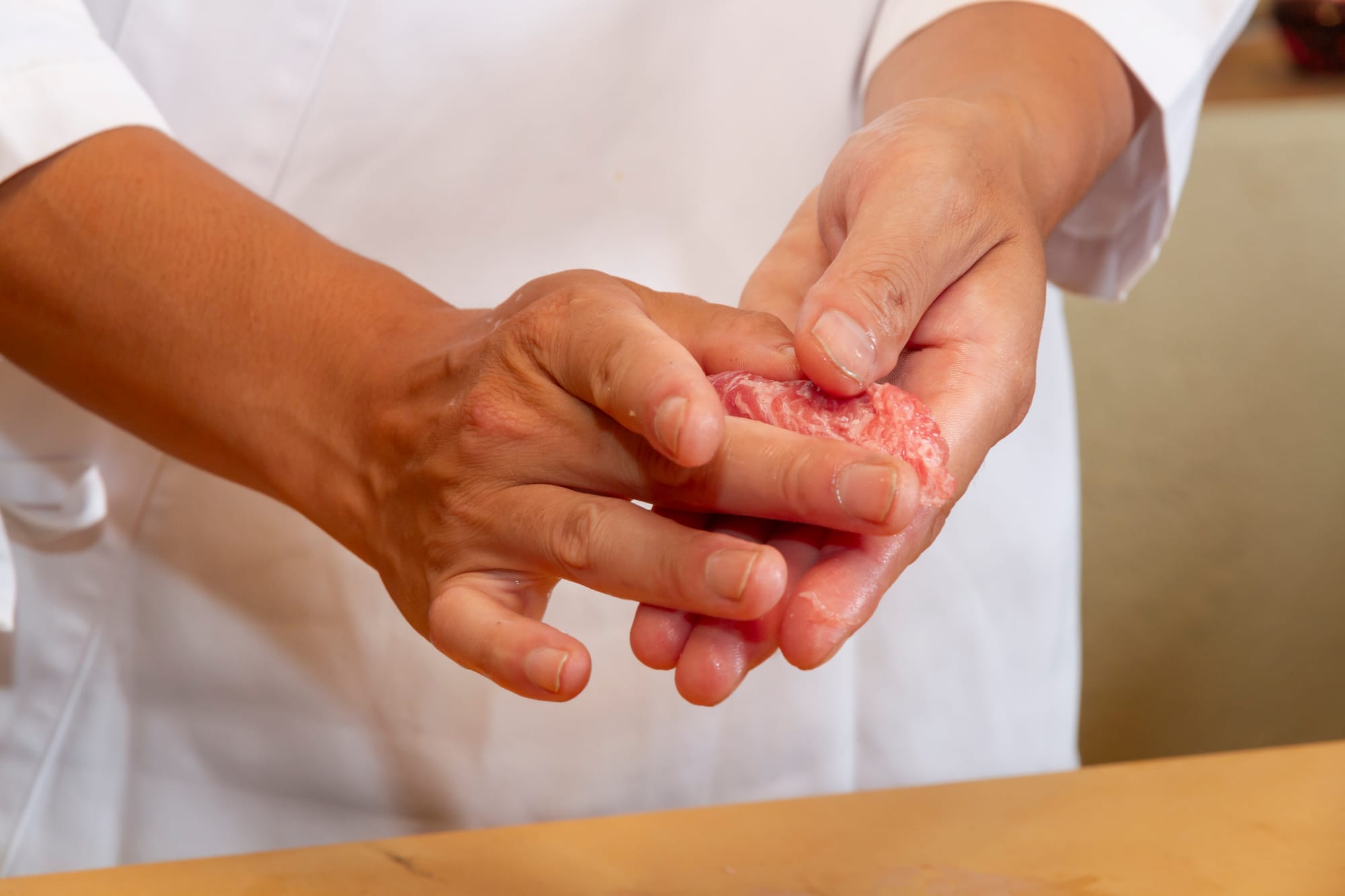 A sushi chef's hands shaping a piece of fatty tuna nigiri, pressing rice and fish together in the palm