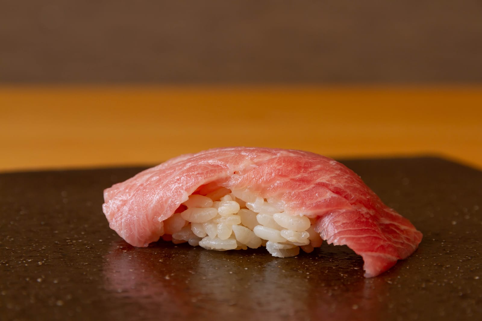 A single piece of fatty tuna nigiri on dark stone, the marbled fish draped over a mound of vinegared rice