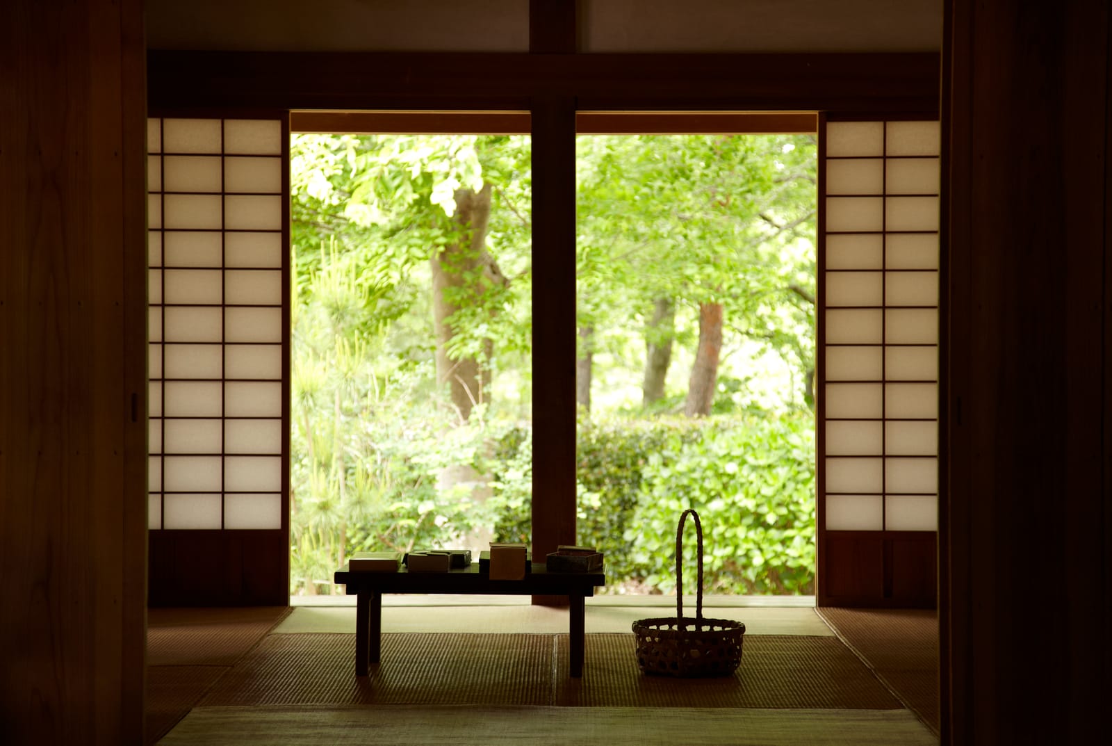 A dim tatami room opening through shoji screens onto a garden, a low table and basket inside