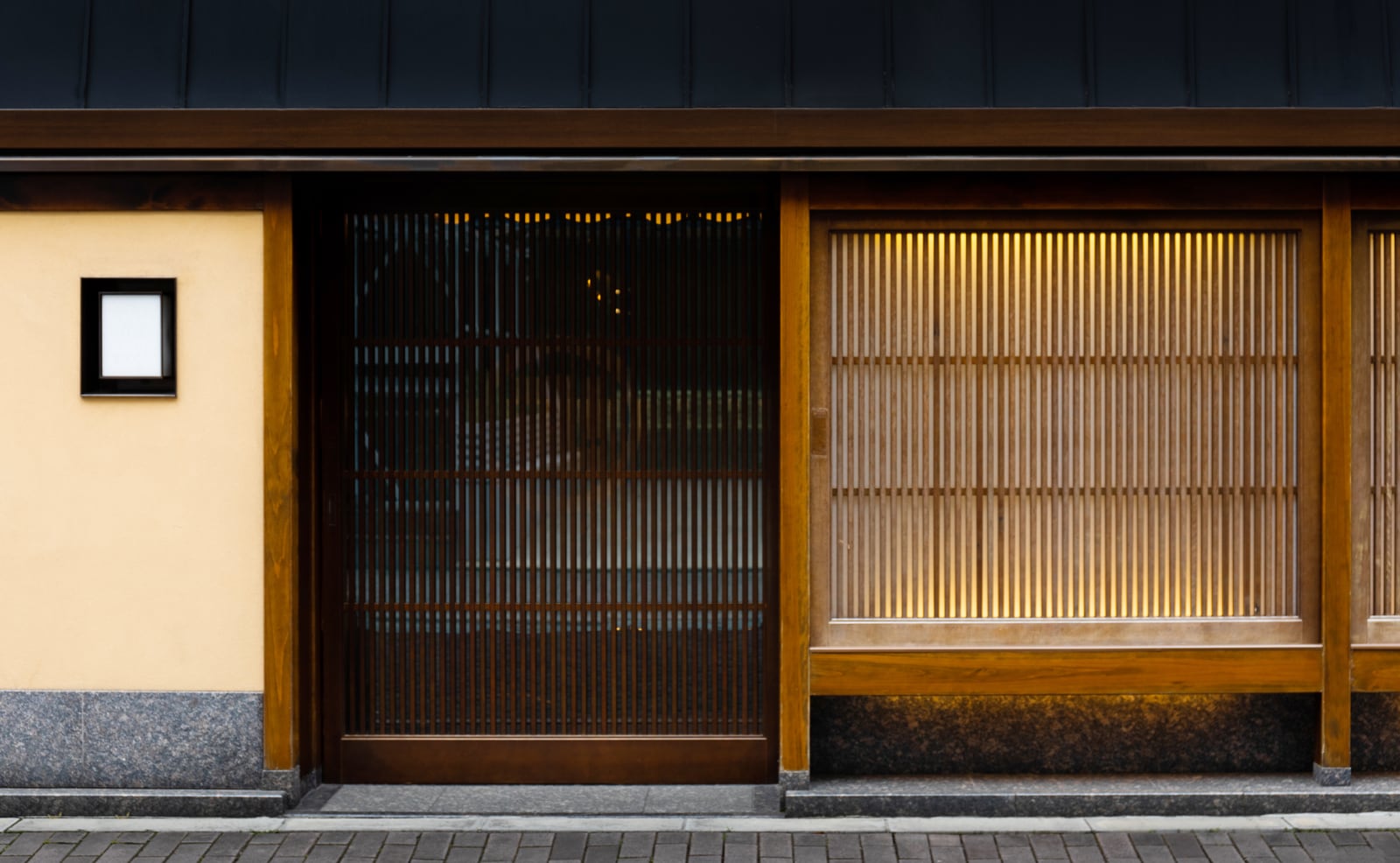 A timber lattice front and sliding door lit warmly from within at dusk, a plastered wall beside it