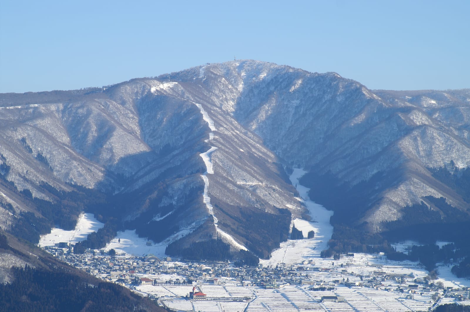The village of Nozawa Onsen in deep snow at the foot of Mount Kenashi, its ski runs cut through the winter forest, Nagano, in January