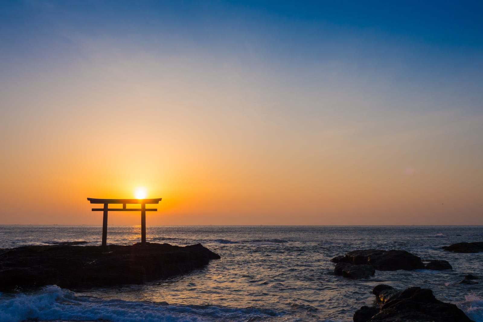 A lone torii silhouetted on a rock in the sea at Ōarai, the sun rising in the opening of the gate above a calm Pacific