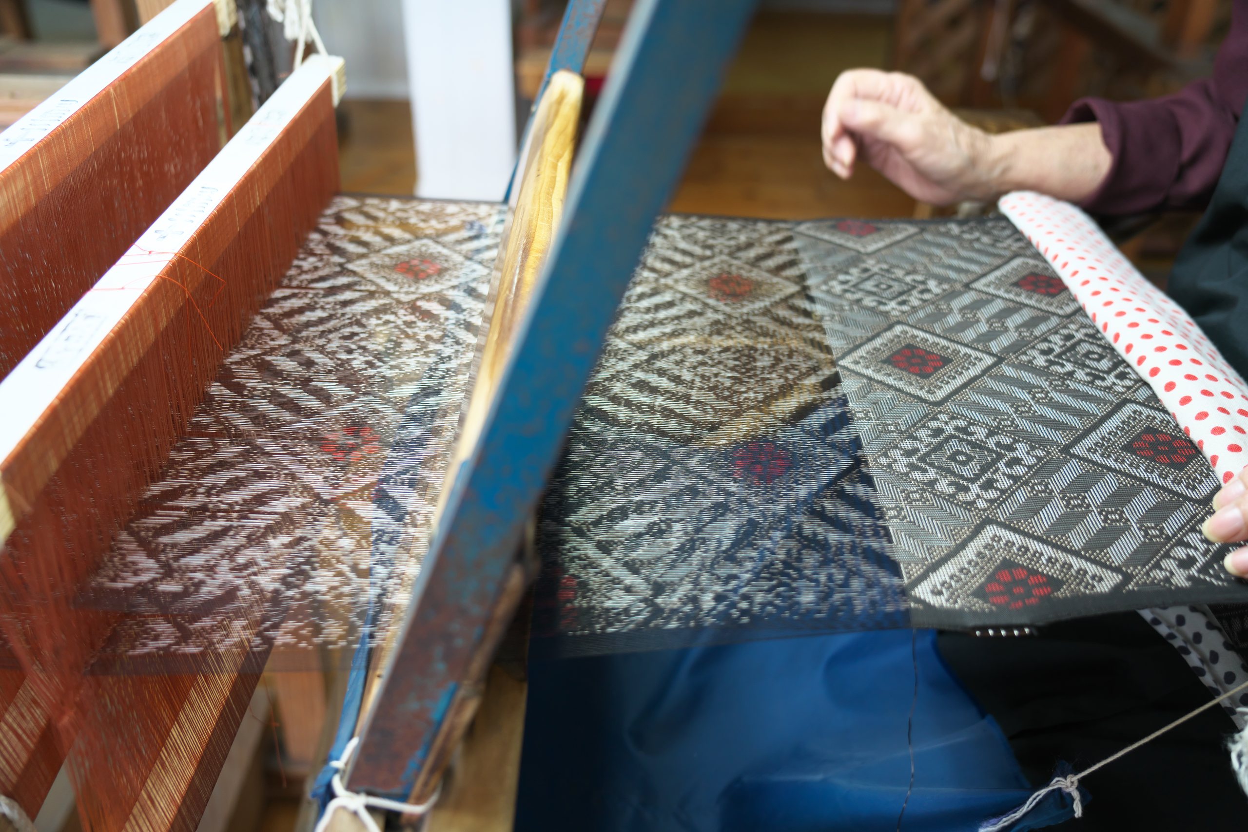 Hands at a loom weaving dark mud-dyed kasuri silk