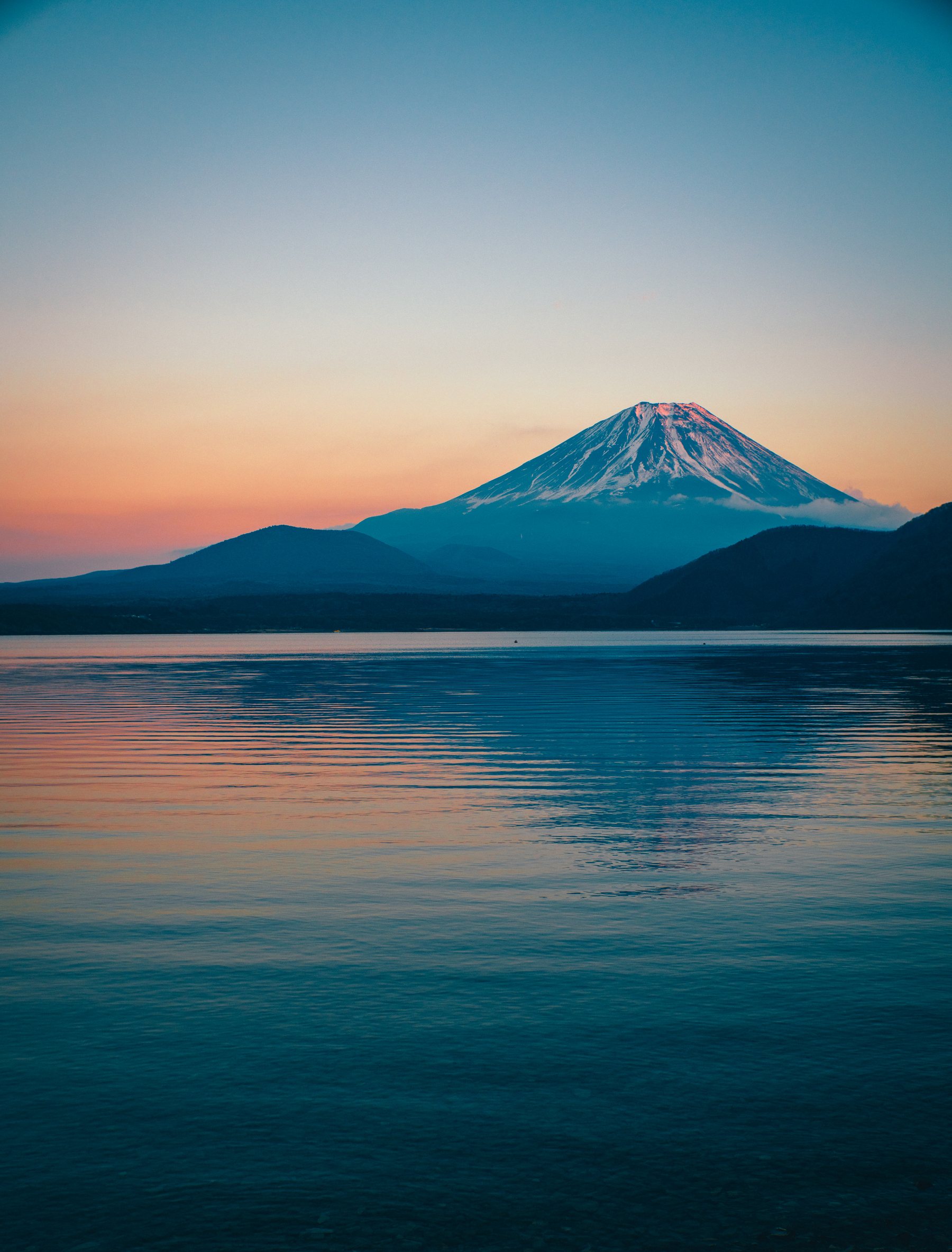 Mount Fuji at dusk across a still lake, snow on its summit and the sky pink and blue above it
