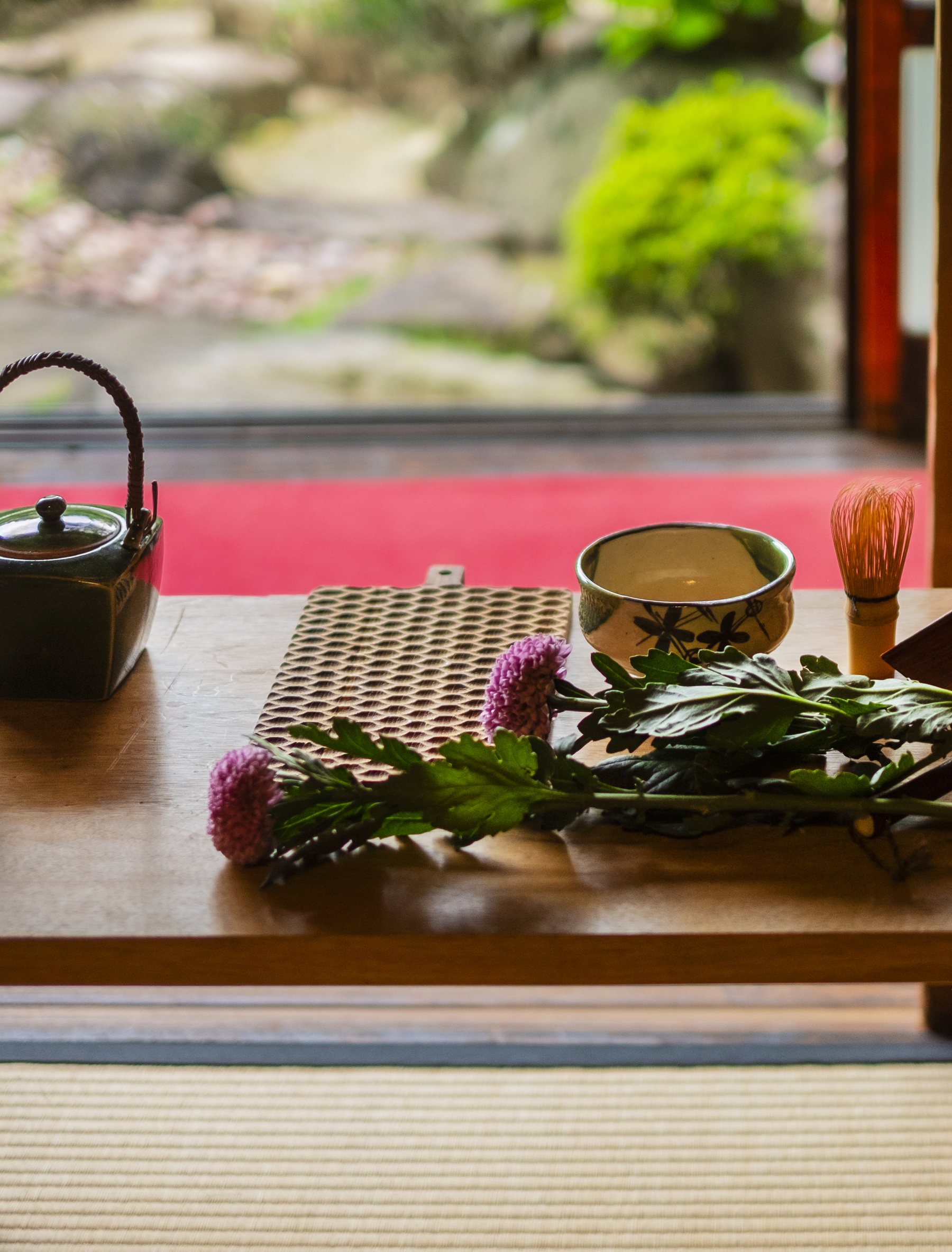An iron kettle, a tea bowl and a bamboo whisk on a wooden table on tatami, a garden beyond the open doors