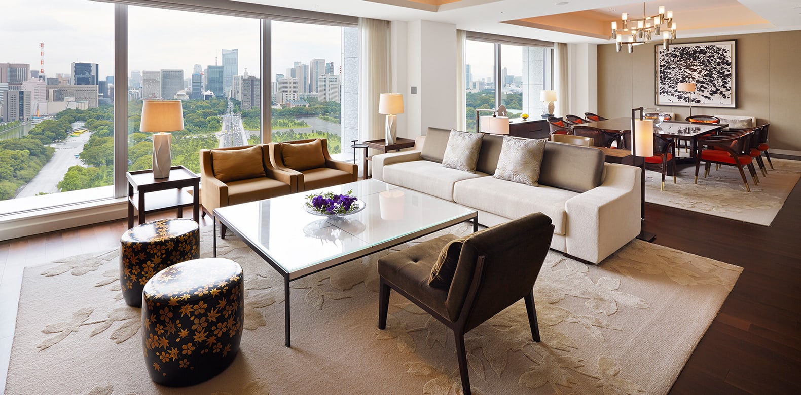 The living room of the Palace Suite at Palace Hotel Tokyo, sofas and armchairs before tall windows onto the palace gardens and the city