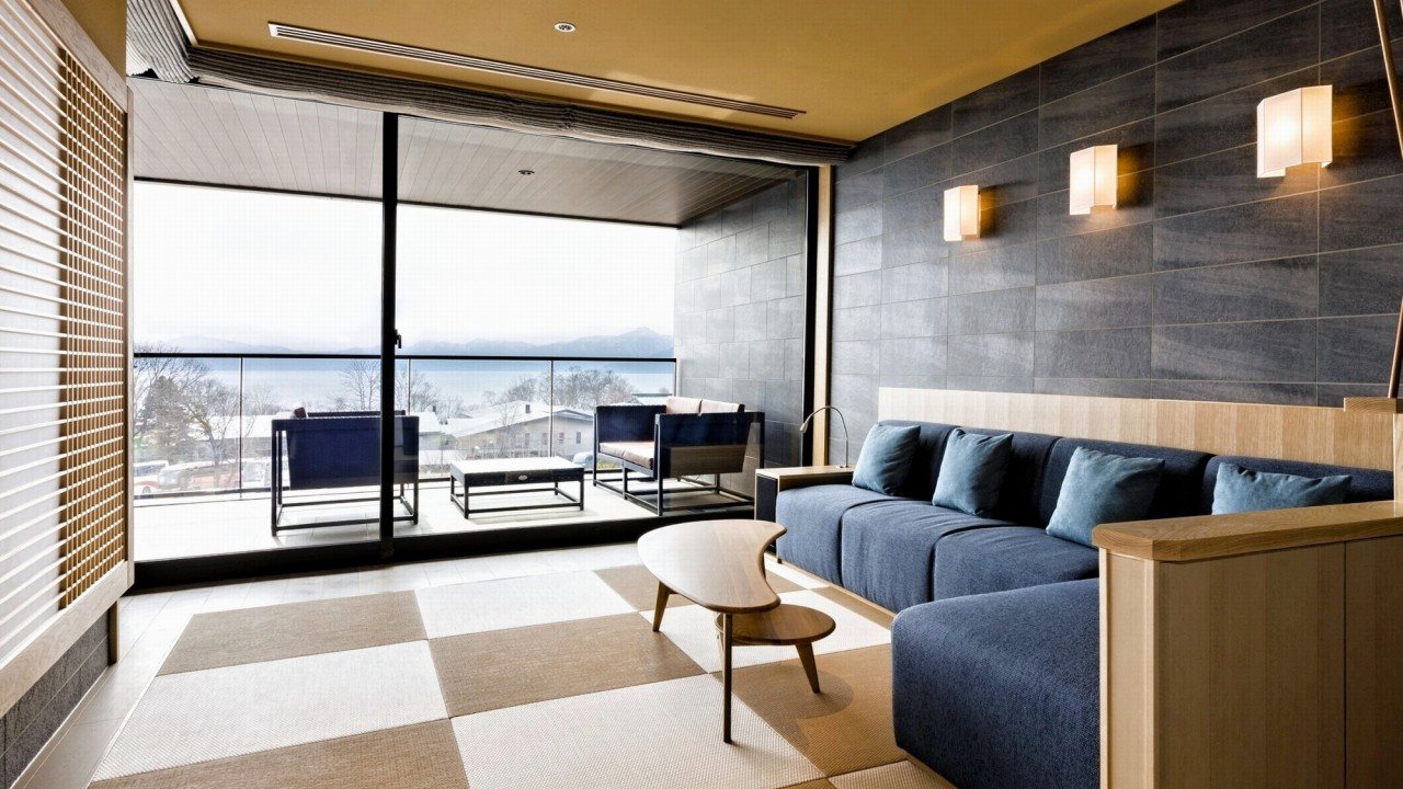 A suite's sitting room at Ao no Za, a blue sofa and low table before glass doors onto the terrace and the lake