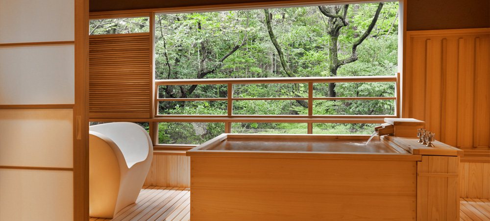 A cypress open-air onsen on a wooden deck beside a window onto green forest, in a garden room at Araya Totoan