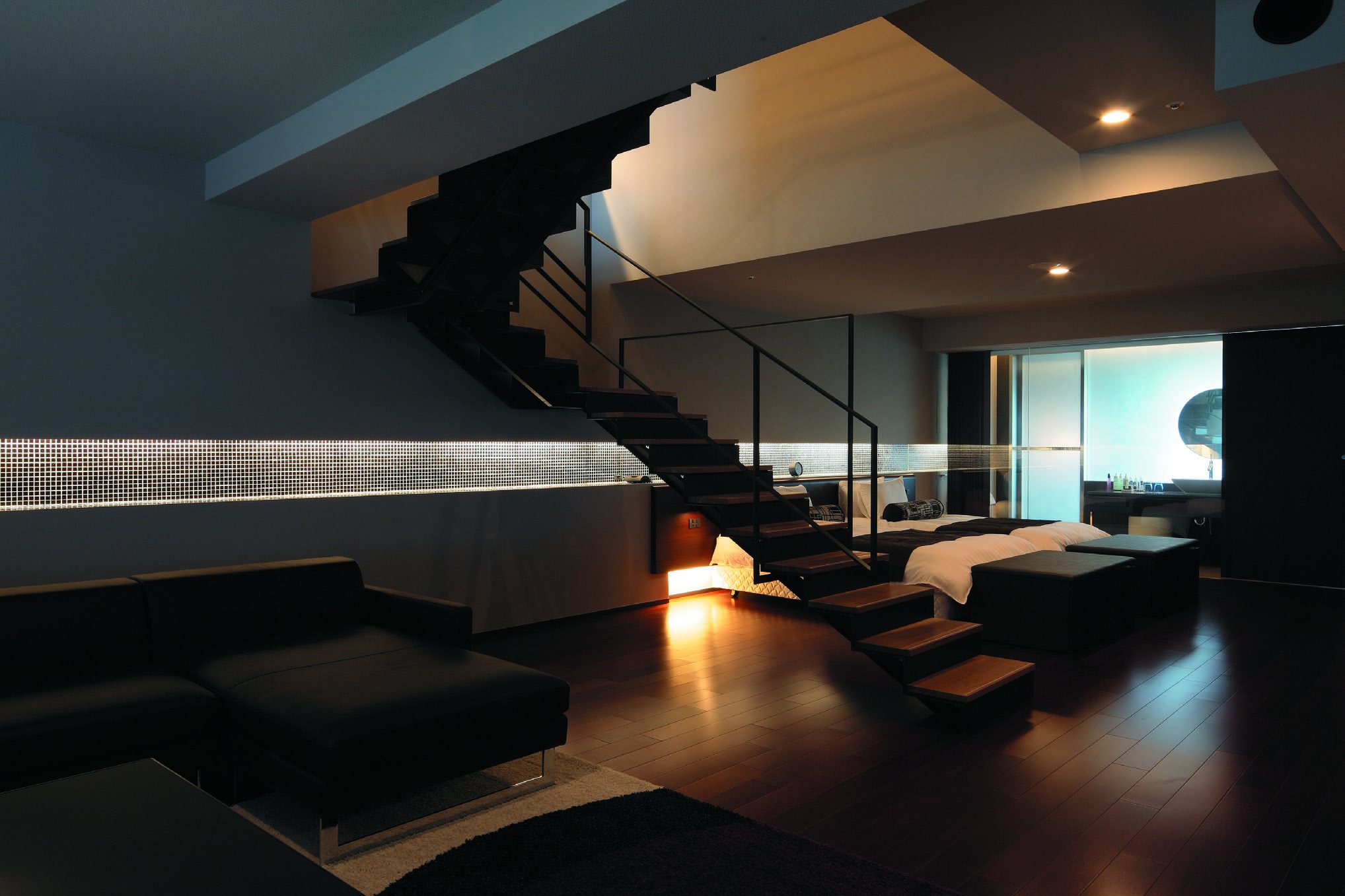 A maisonette suite, a staircase rising from a dark sitting room to a sleeping floor by the window