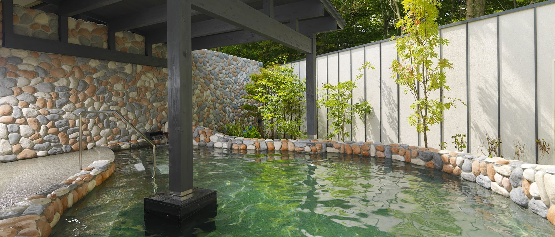 An open-air onsen in stone among trees and rocks at Epuy, Onuma