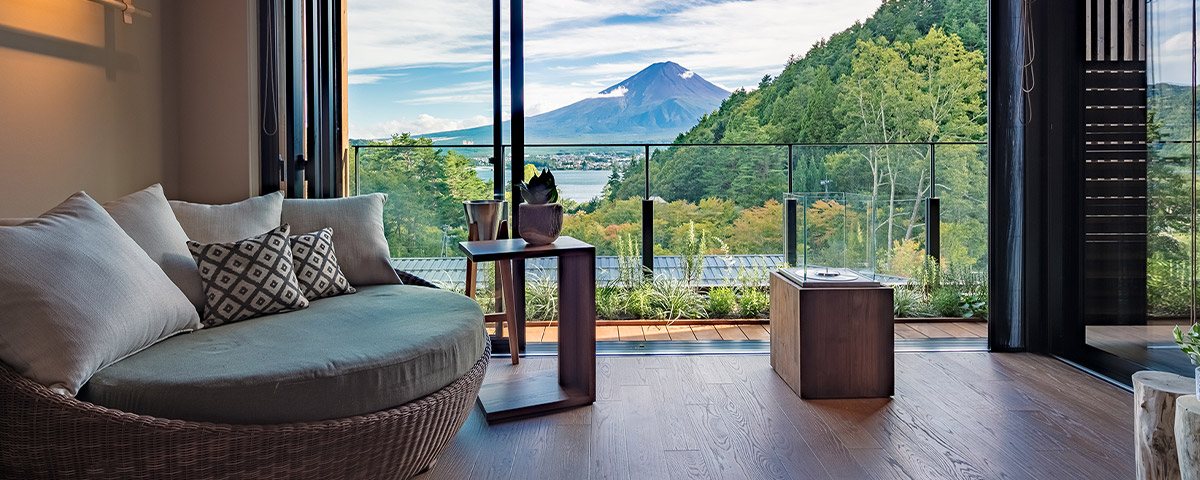 A curved sofa in a suite at FUFU Kawaguchiko, glass doors open onto a terrace and Mount Fuji beyond the trees