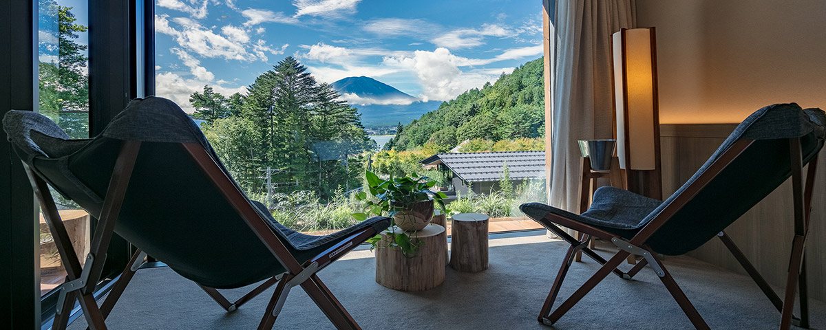 Two sling chairs on a suite's terrace, Mount Fuji rising beyond the forest