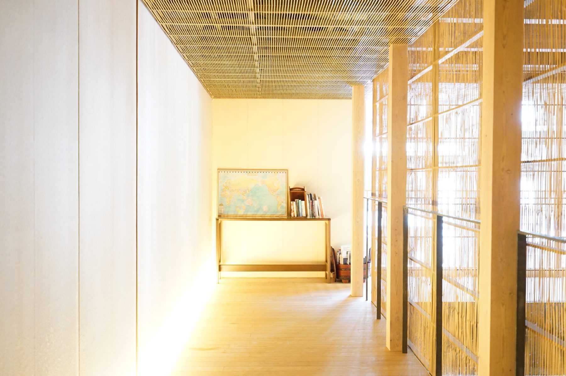 A pale corridor at Fujiya, sunlight falling through screens of bamboo lattice onto a wooden floor