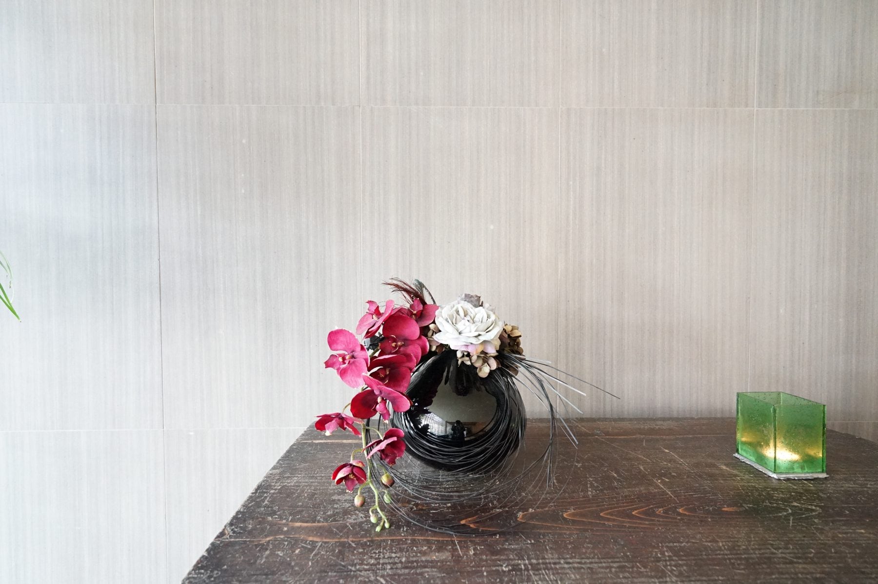 Red orchids in a round black vase on an old wooden table, a pale plaster wall behind