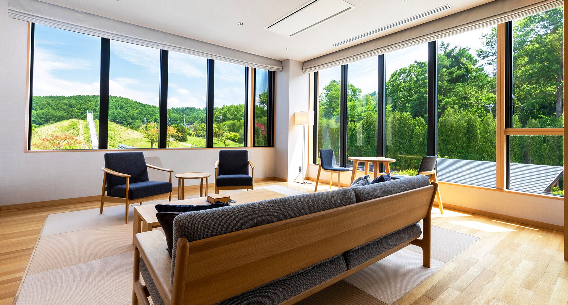 A sitting room with sofas before a wall of glass onto the trees and Lake Toya below, at Hikari no Uta