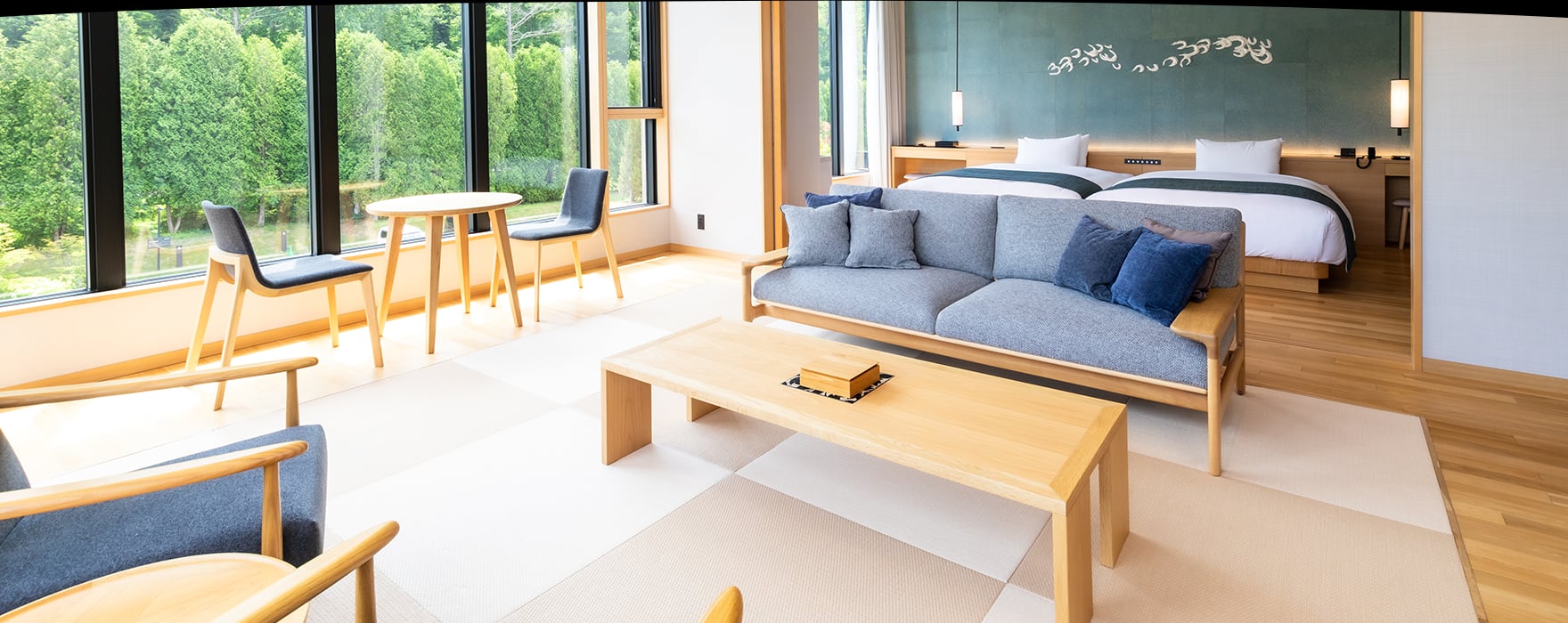 A room of pale wood and tatami, a sofa, twin beds beyond, windows onto the trees