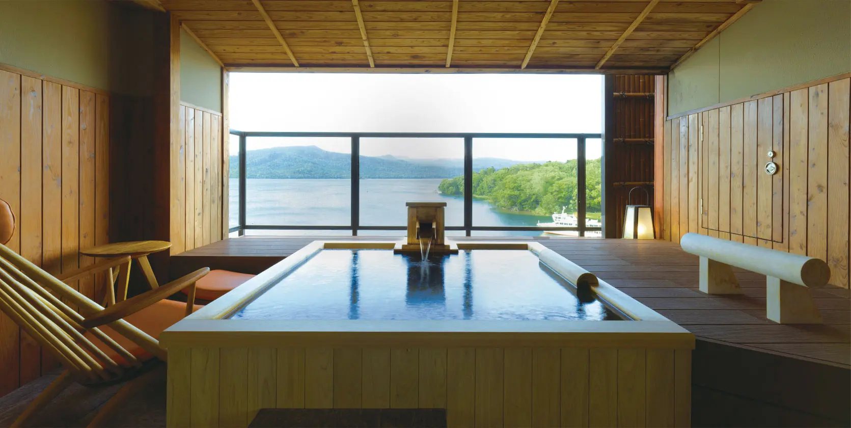 An onsen pool in a timbered room open to Lake Akan, a wooded island and the far shore beyond