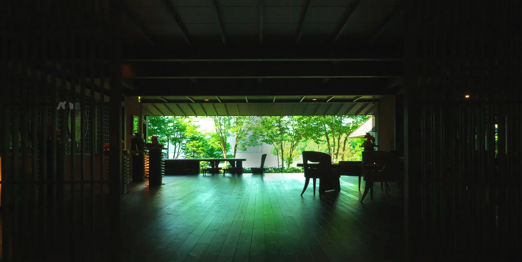 A dark timbered hall opening at the far end onto bright green forest, at Hinanoza