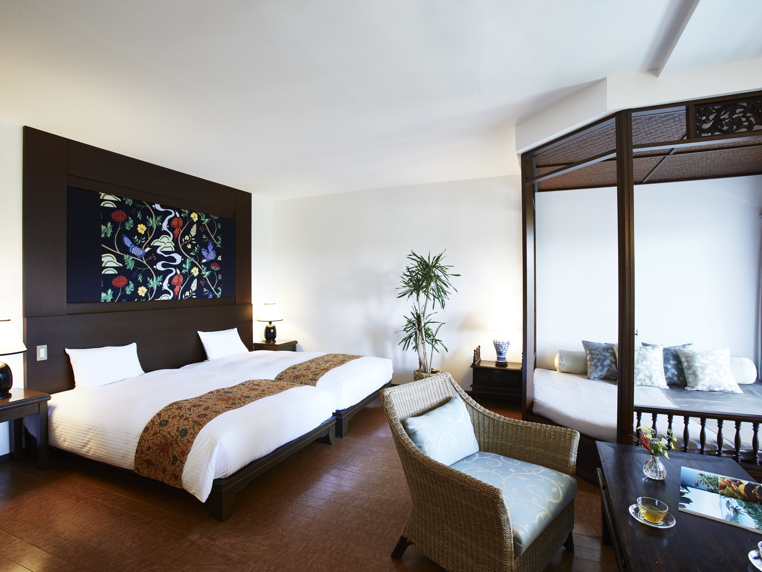 A twin room with dark wood floors, a woven armchair and a canopy over the sitting area