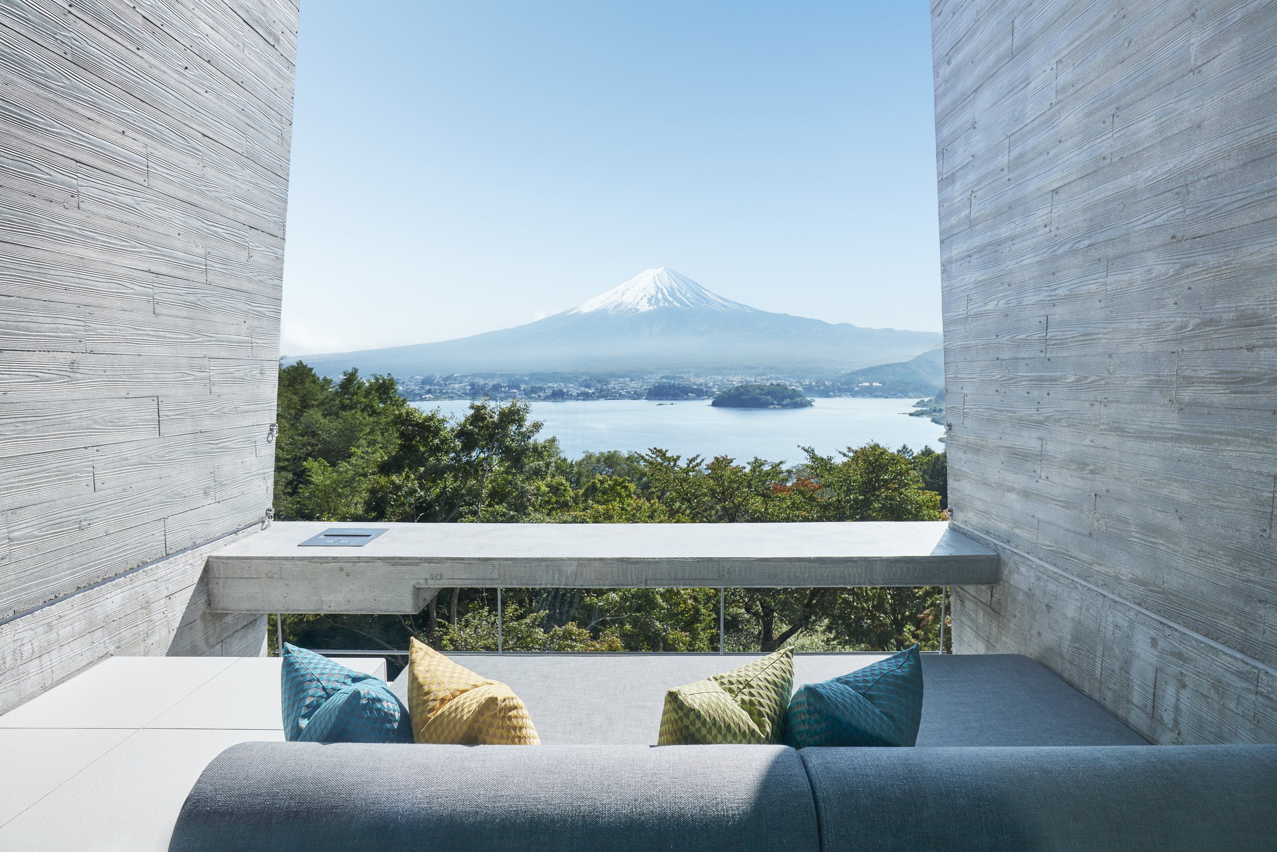 A long sofa on a concrete terrace between two walls, Mount Fuji and the lake beyond