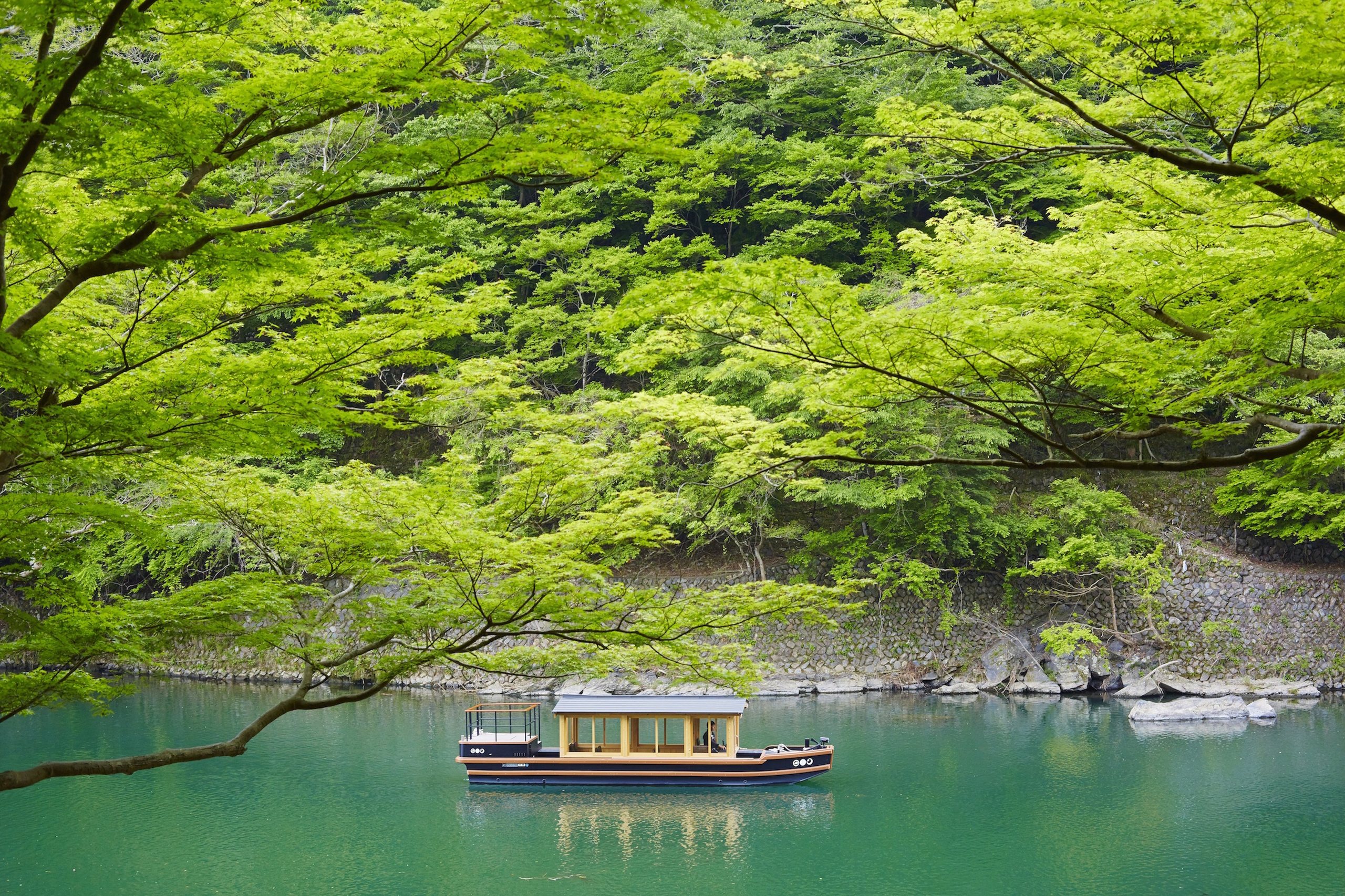 A wooden boat on the green river beneath maple trees