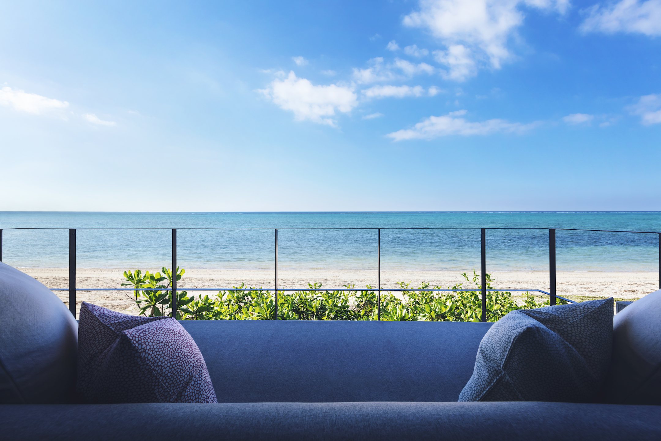 A deep sofa on a terrace above the sea, white sand and blue water beyond