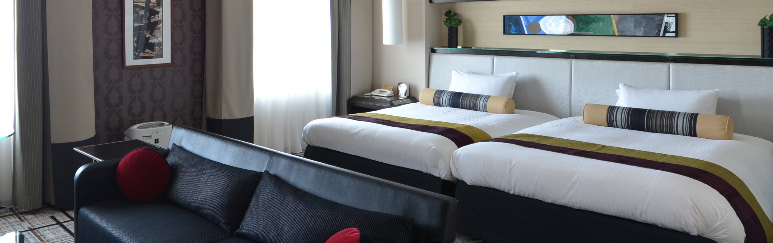 A deluxe twin room, two beds with gold runners and a black leather sofa by the window