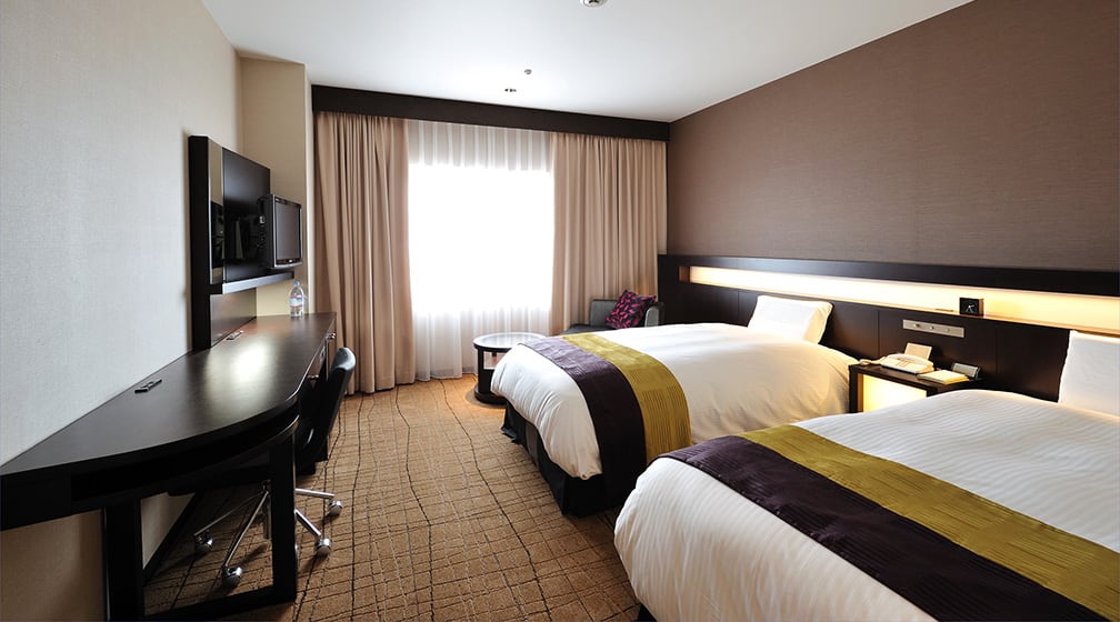 A twin room with a long curved desk and two beds by the window