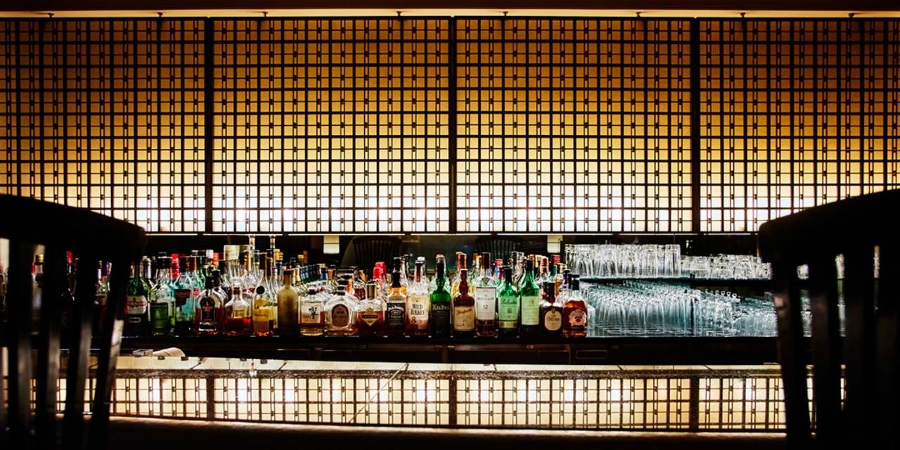 A bar backlit by a tall lattice screen, its bottles and glasses in a line of warm light