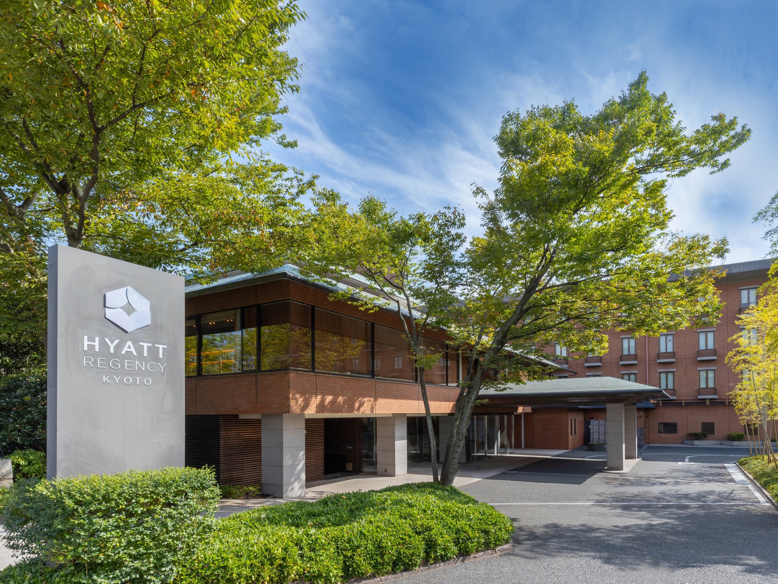The hotel's low red-brick wings among tall trees, its sign at the drive, beneath a blue sky