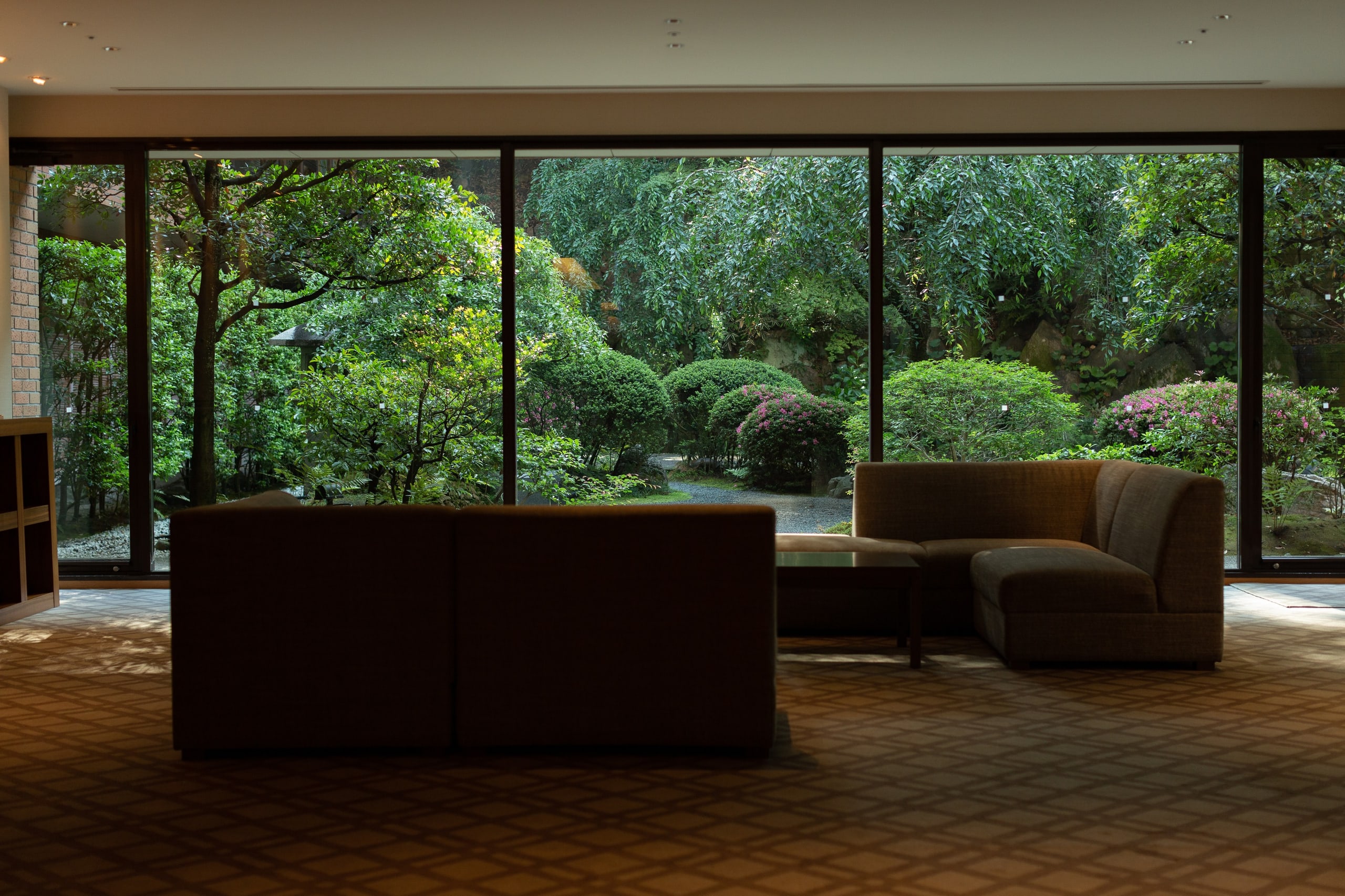 A lounge of deep sofas before a wall of glass onto the garden