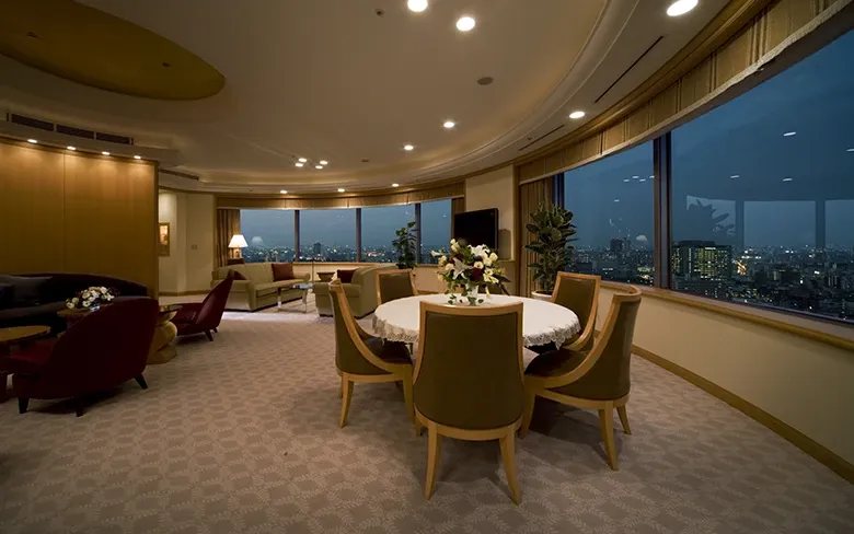 A corner suite on the Imperial Floor at night, a round dining table beneath a sweep of windows onto the lit city