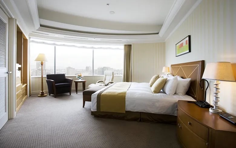 A suite bedroom by day, a wide bed facing a window and two armchairs