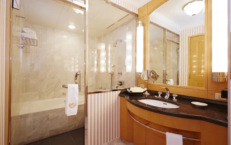 A marble bathroom with a glass-walled shower and bath, a wide vanity and towels laid out