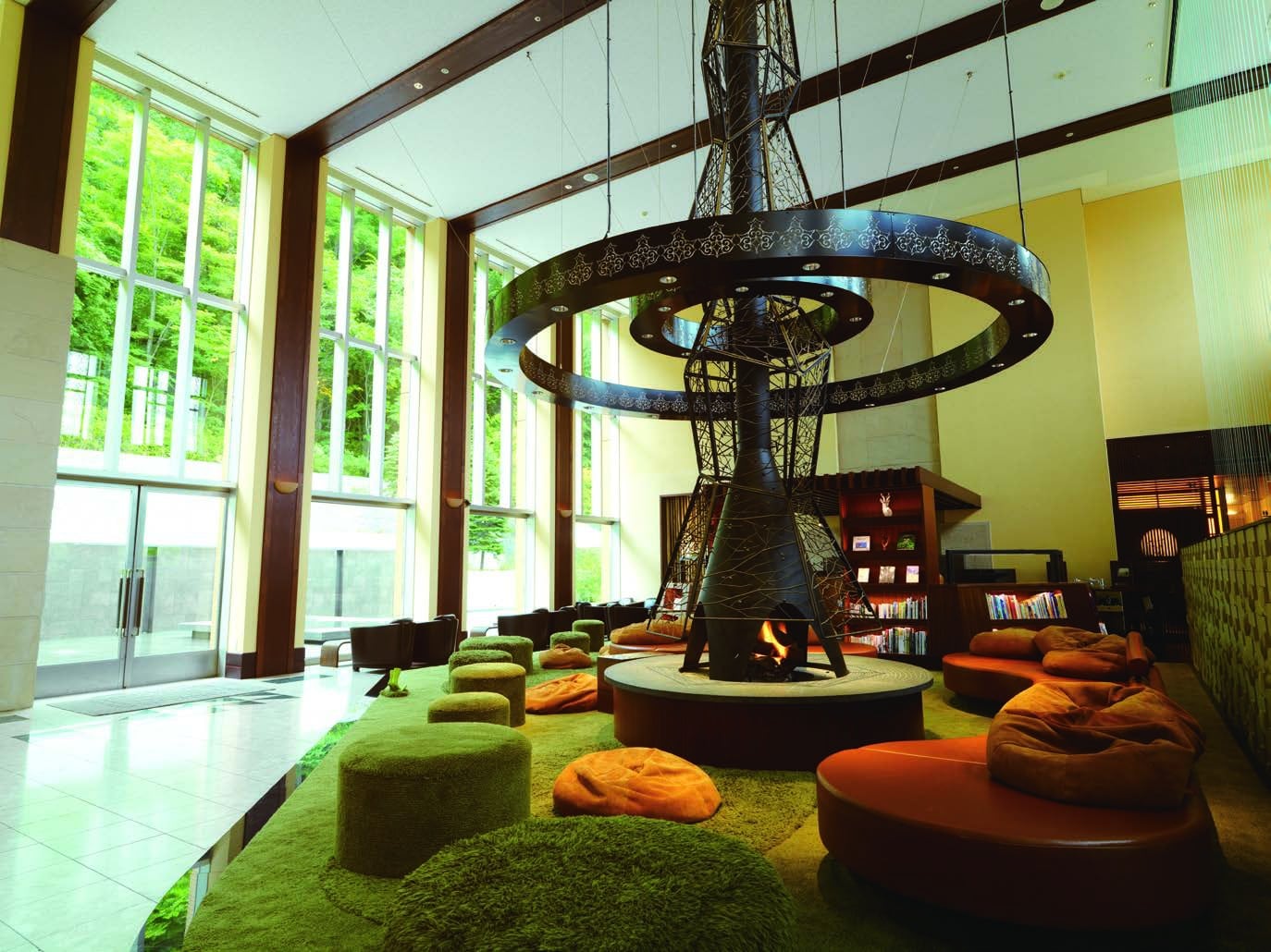 A lounge under tall windows onto the forest, a hanging hearth above a circle of low seats on a moss-green carpet